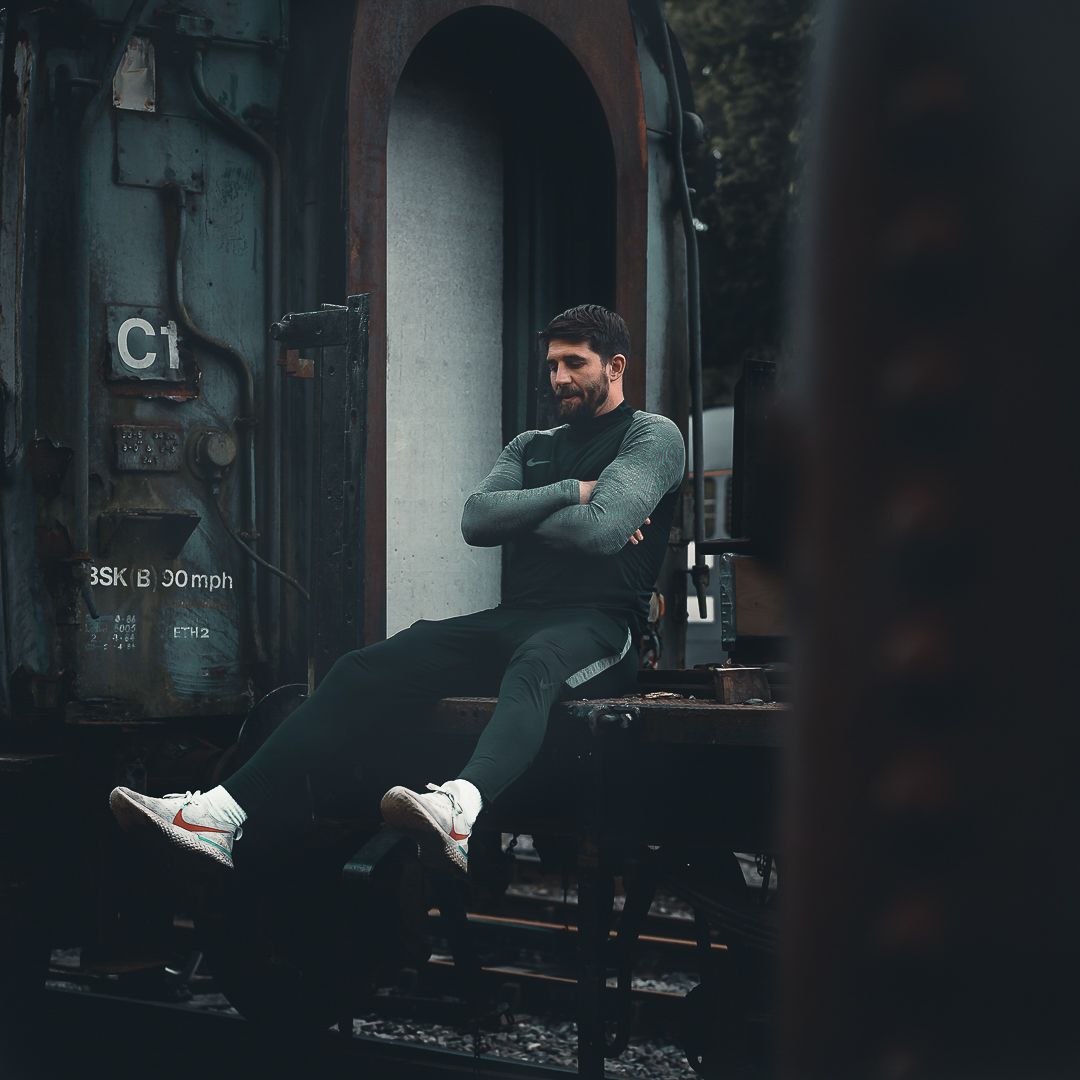 Man in grey athletic wear sitting relaxed on vintage train car on railway tracks.