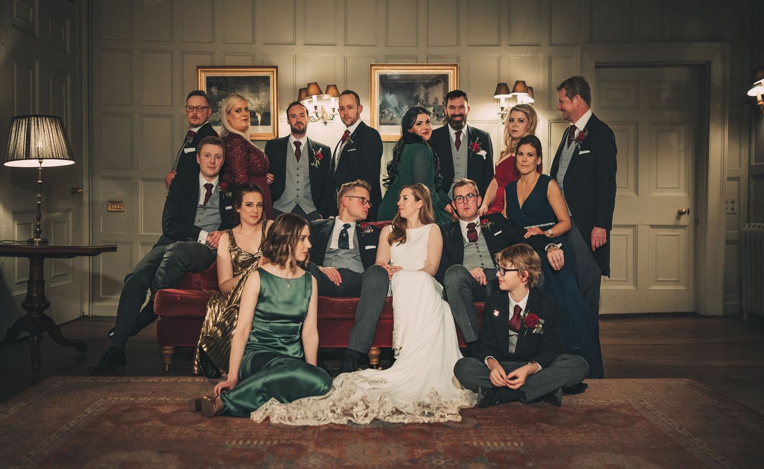 Large wedding party poses together in an elegant room, bride and groom centered among family and friends.