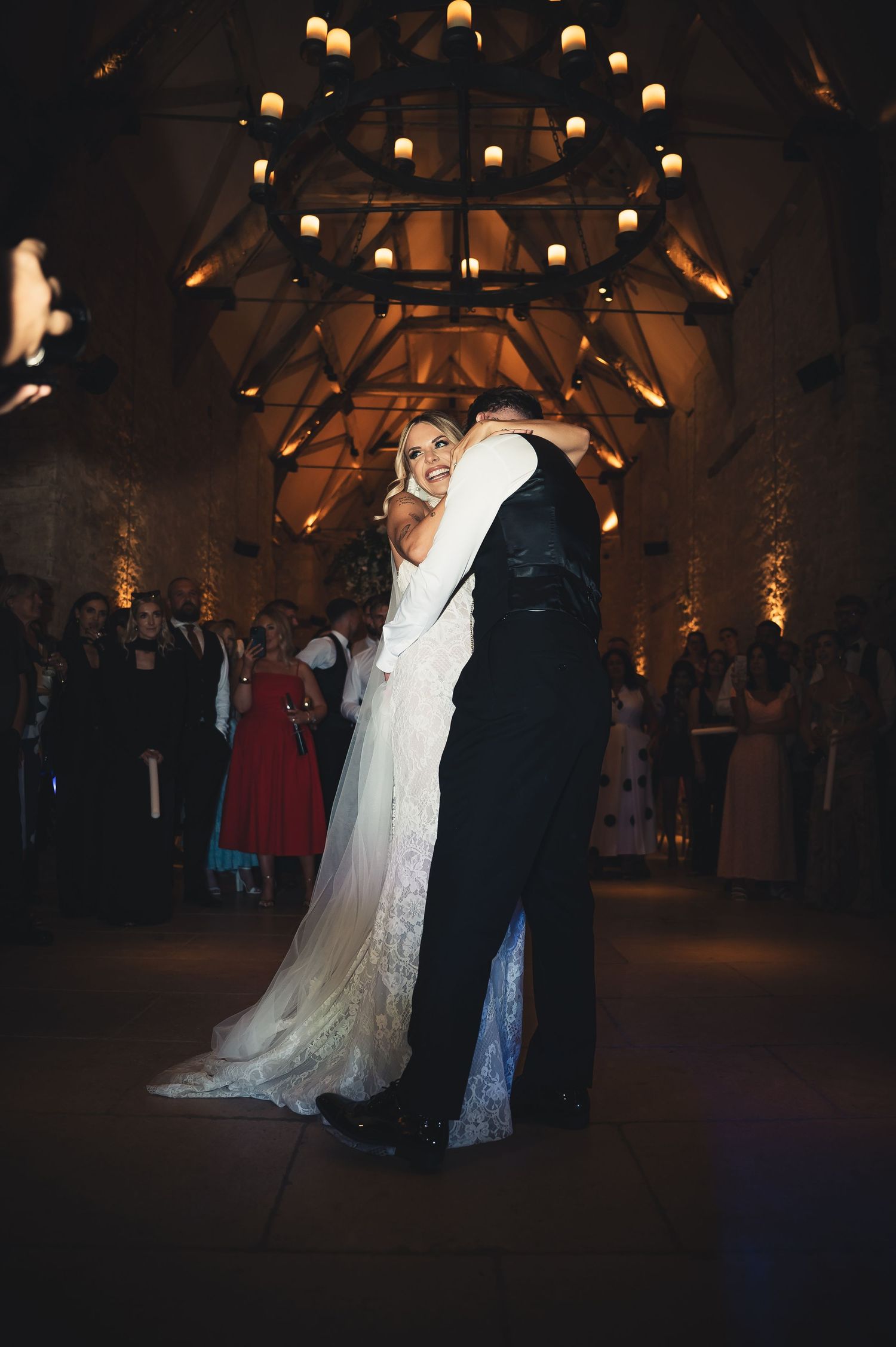Bride and groom share their first dance under a chandelier in a warmly lit stone venue.
