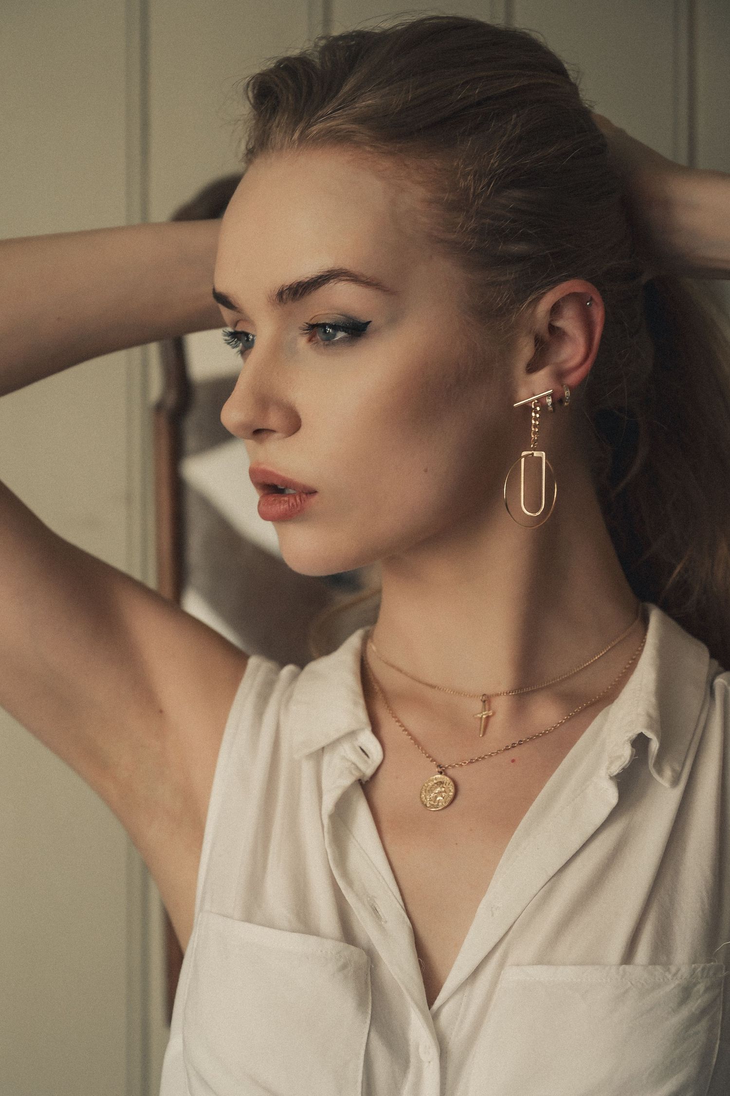 Close-up of woman wearing gold chain earrings and layered gold necklaces with a white sleeveless shirt.