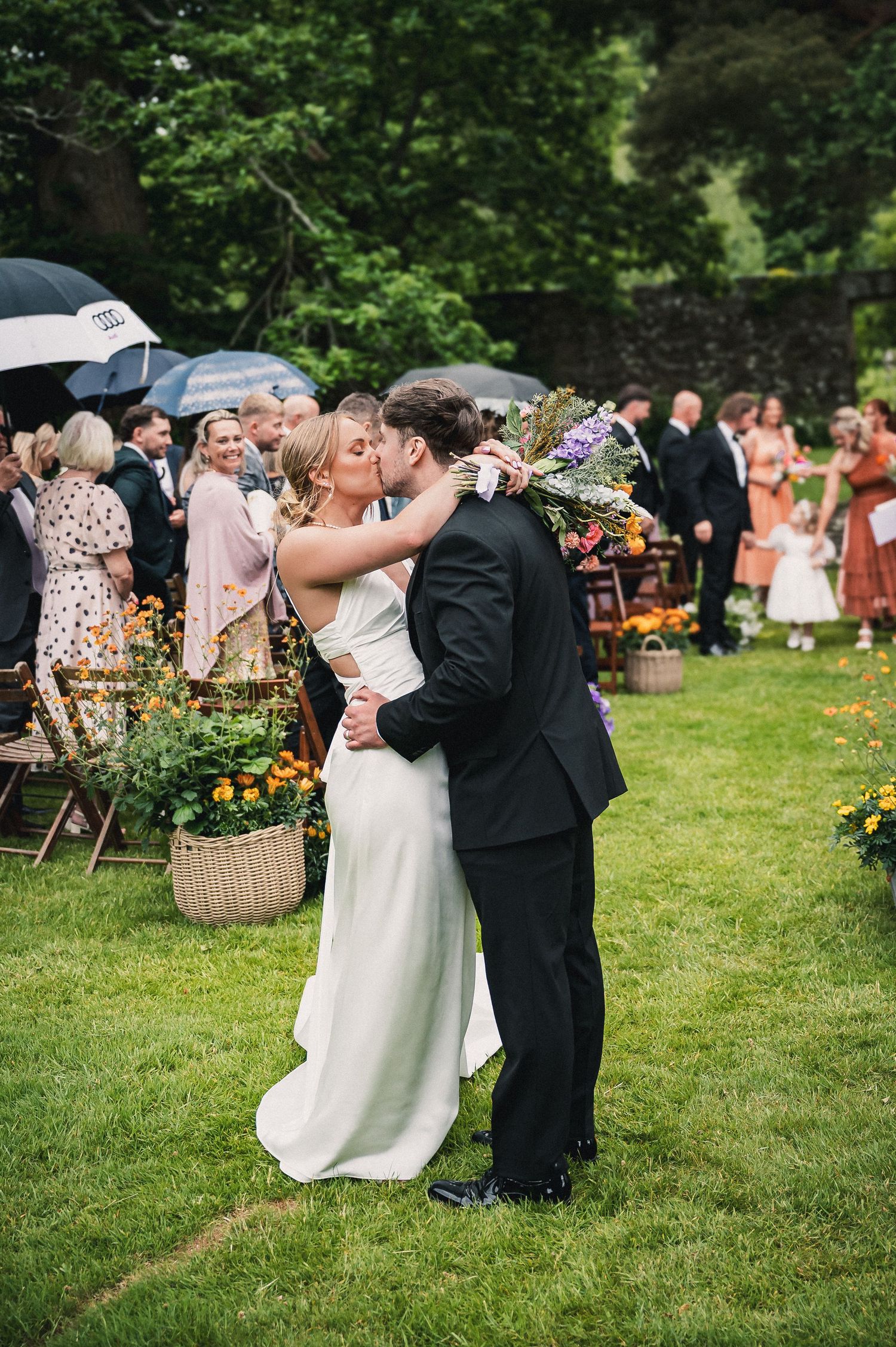 Bride and groom share a first kiss on the lawn during an outdoor garden wedding ceremony.