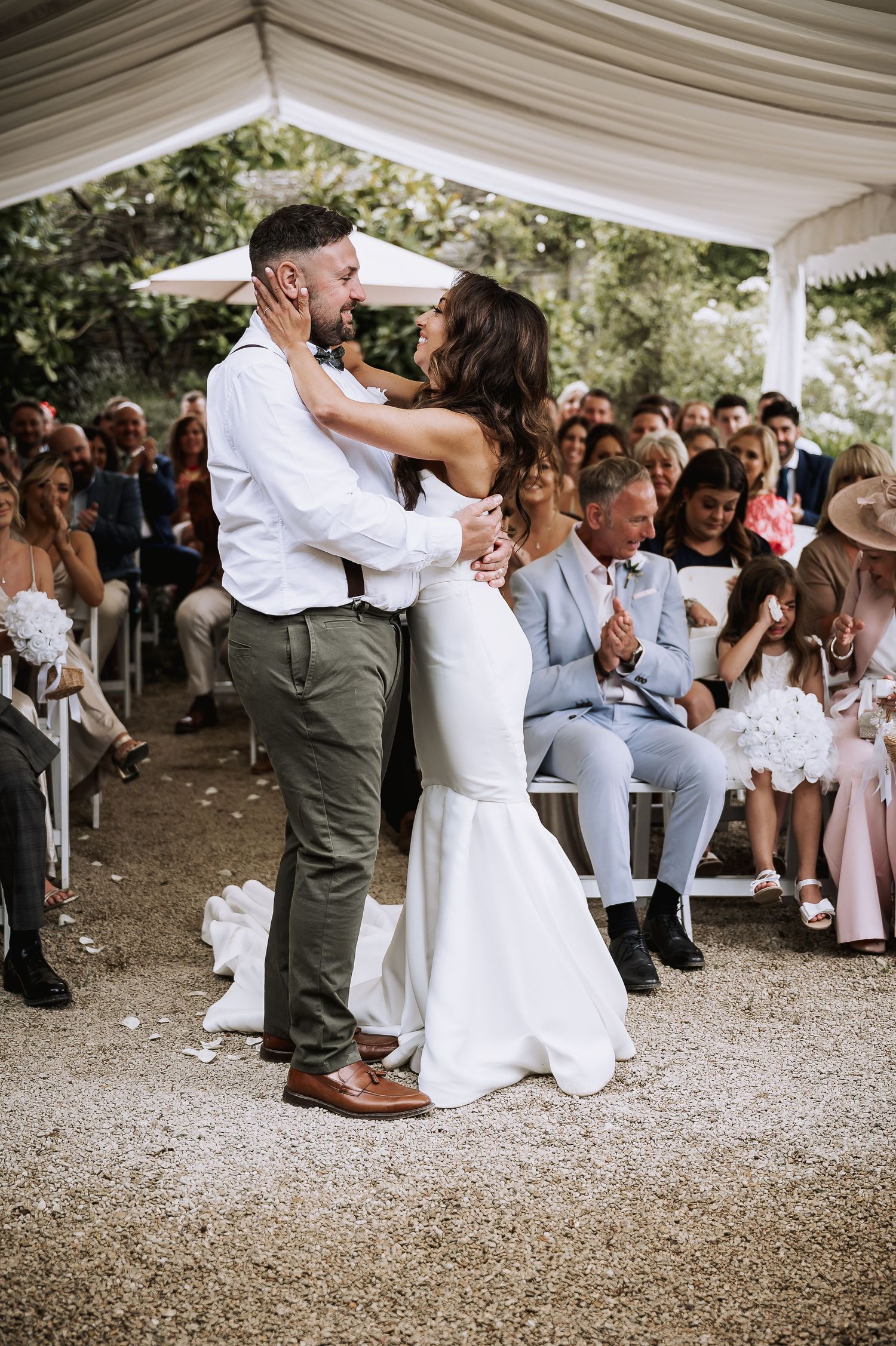 Bride and groom embrace joyfully after their outdoor wedding ceremony under a white marquee.