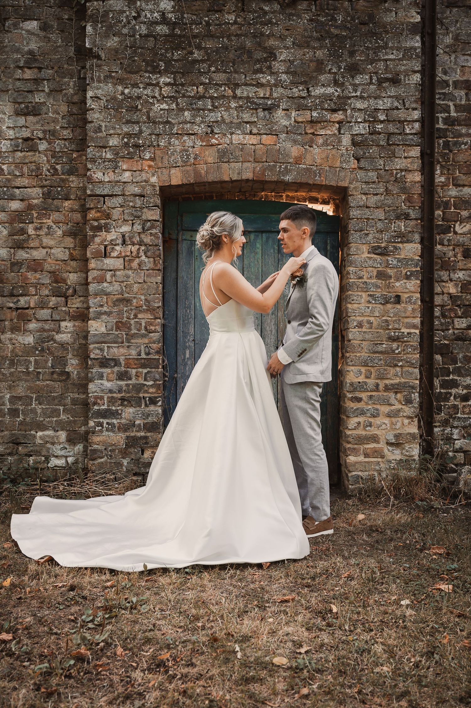 Bride and groom sharing intimate moment before rustic blue door set in aged brick wall.