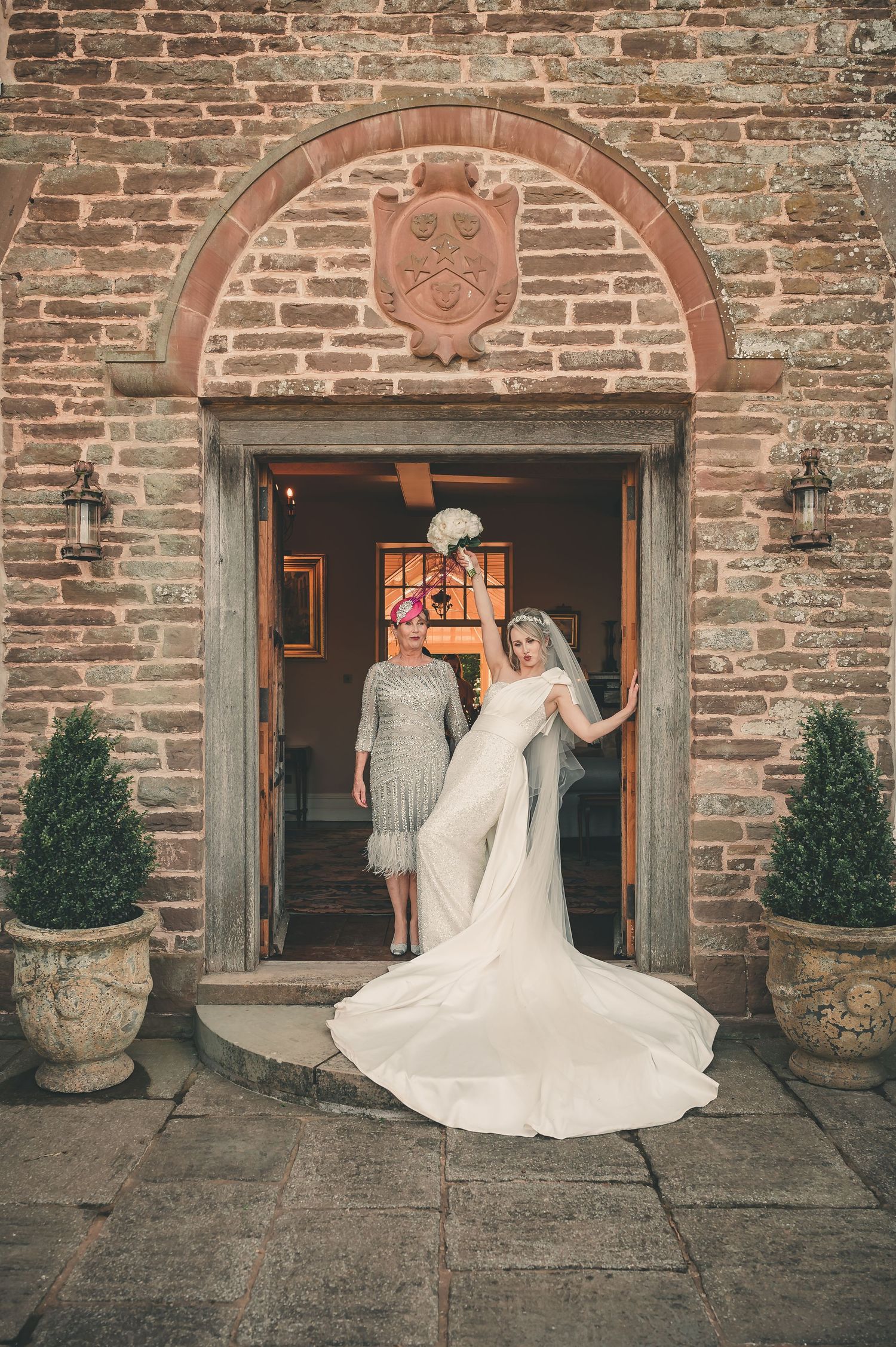 Elegant bride in fitted gown with long train standing in stone archway doorway.