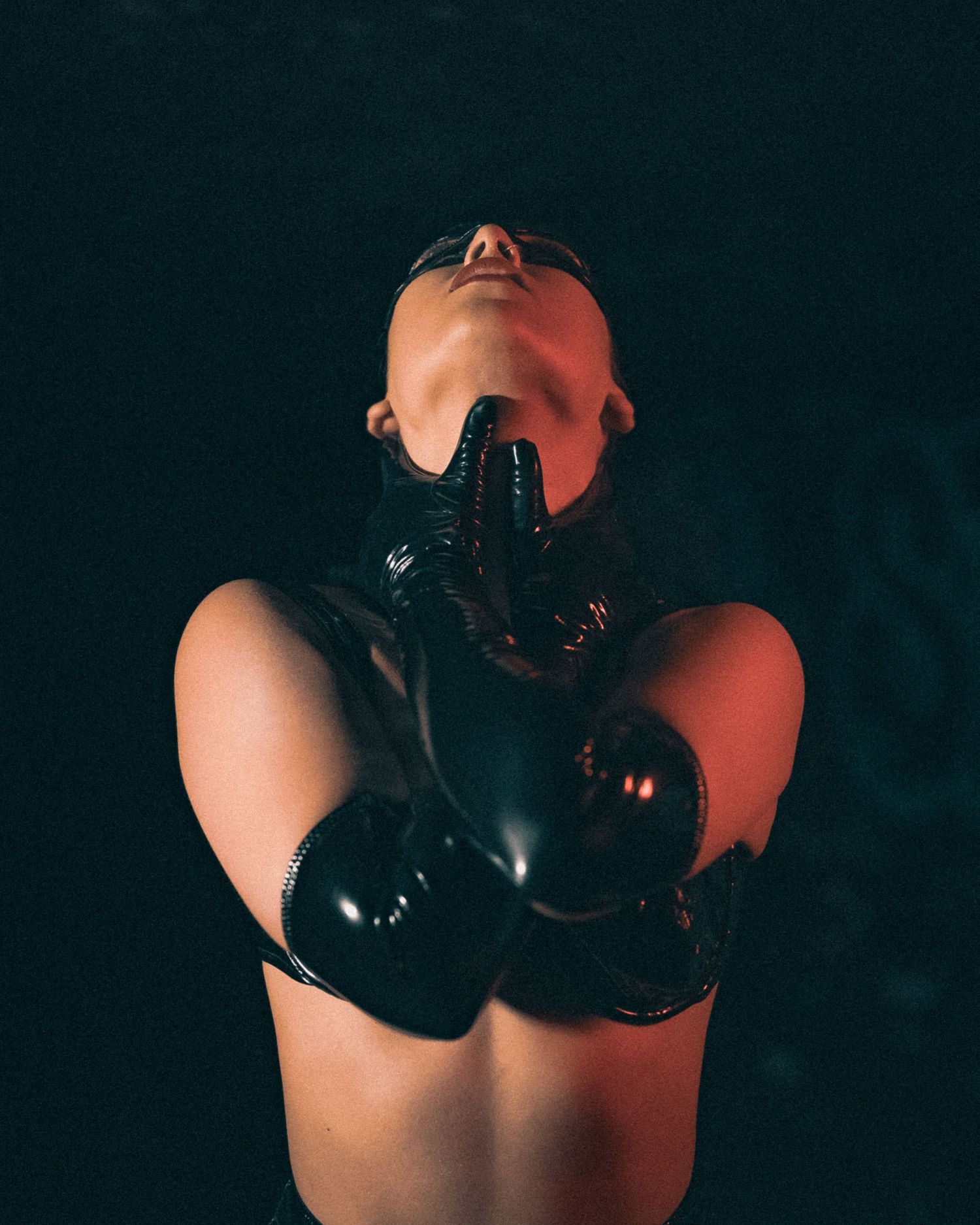 Woman in black latex gloves pointing fingers toward camera against dark background.
