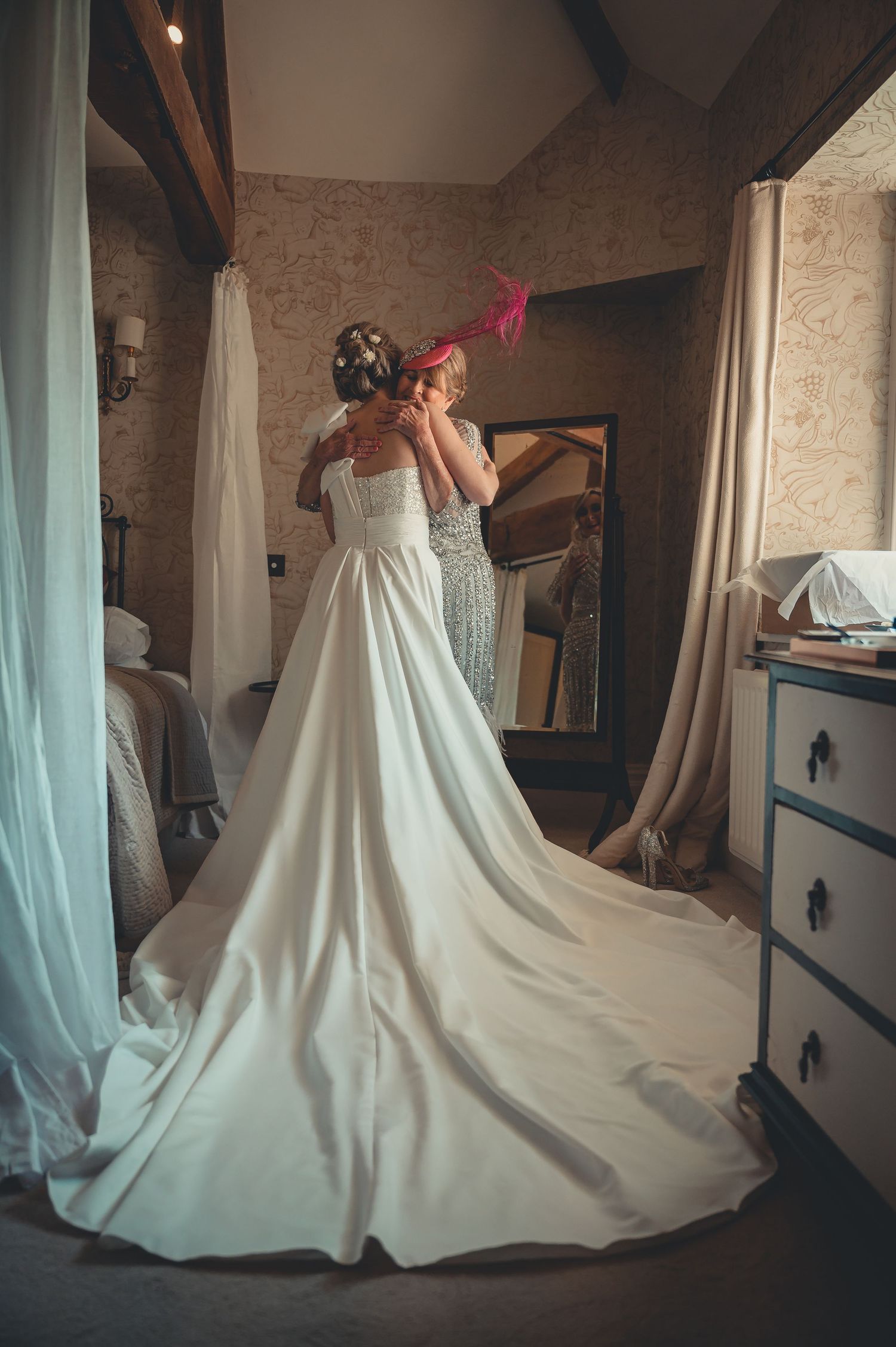 Bride in full-length white gown with long train getting ready in rustic bedroom.