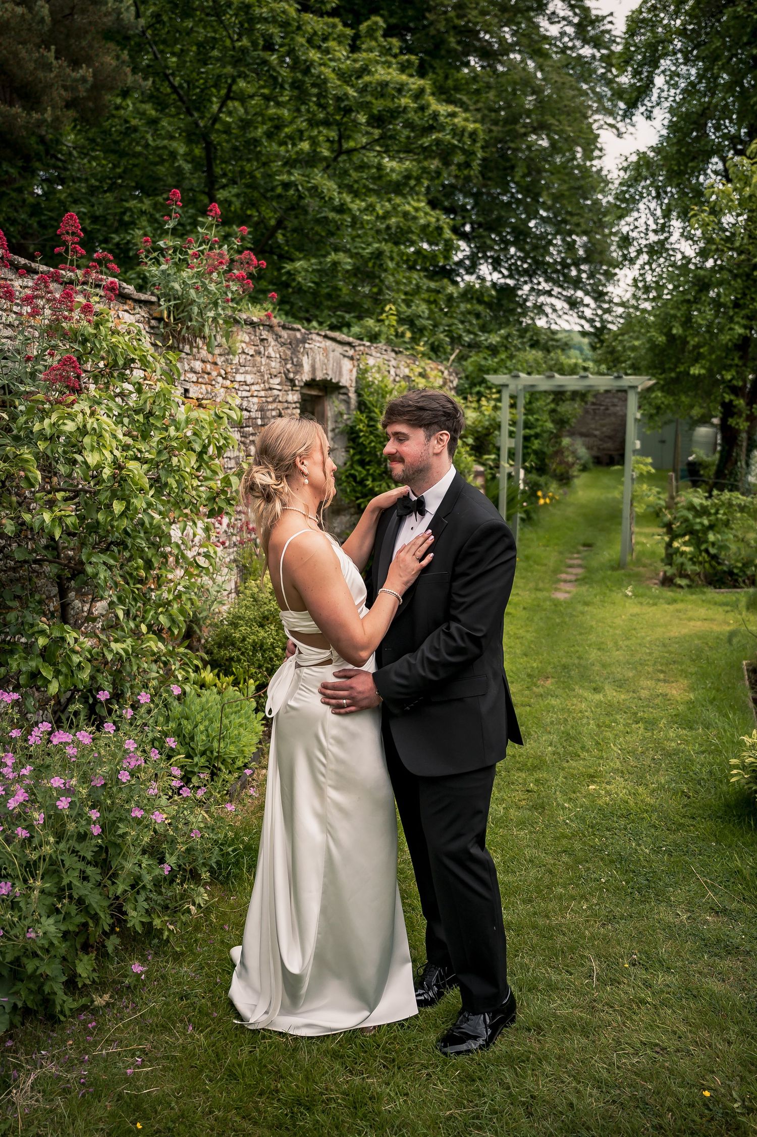 Bride and groom sharing a tender moment in a lush walled garden surrounded by colorful blooms.