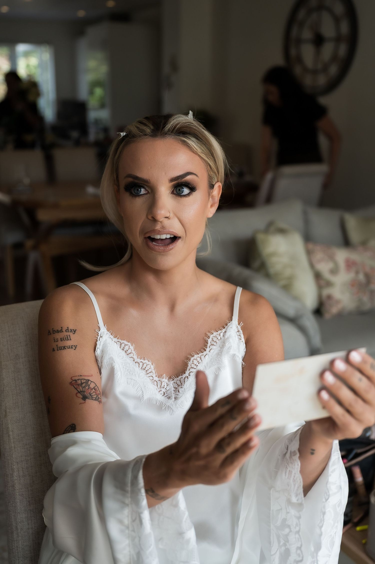 Blonde bride in a white robe reading a letter with surprise expression before her wedding.