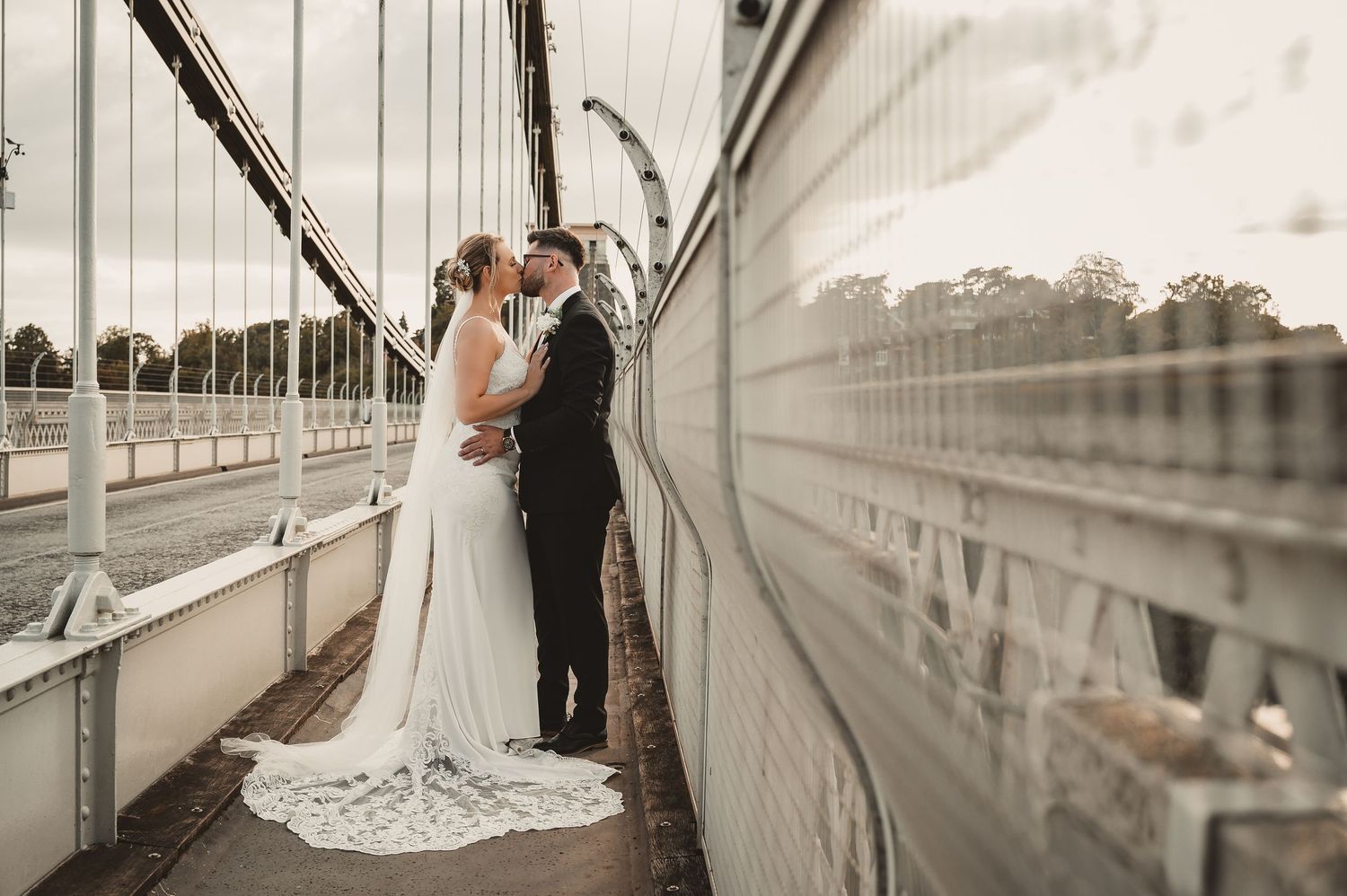 Bride and groom sharing a romantic kiss on a suspension bridge on their wedding day.