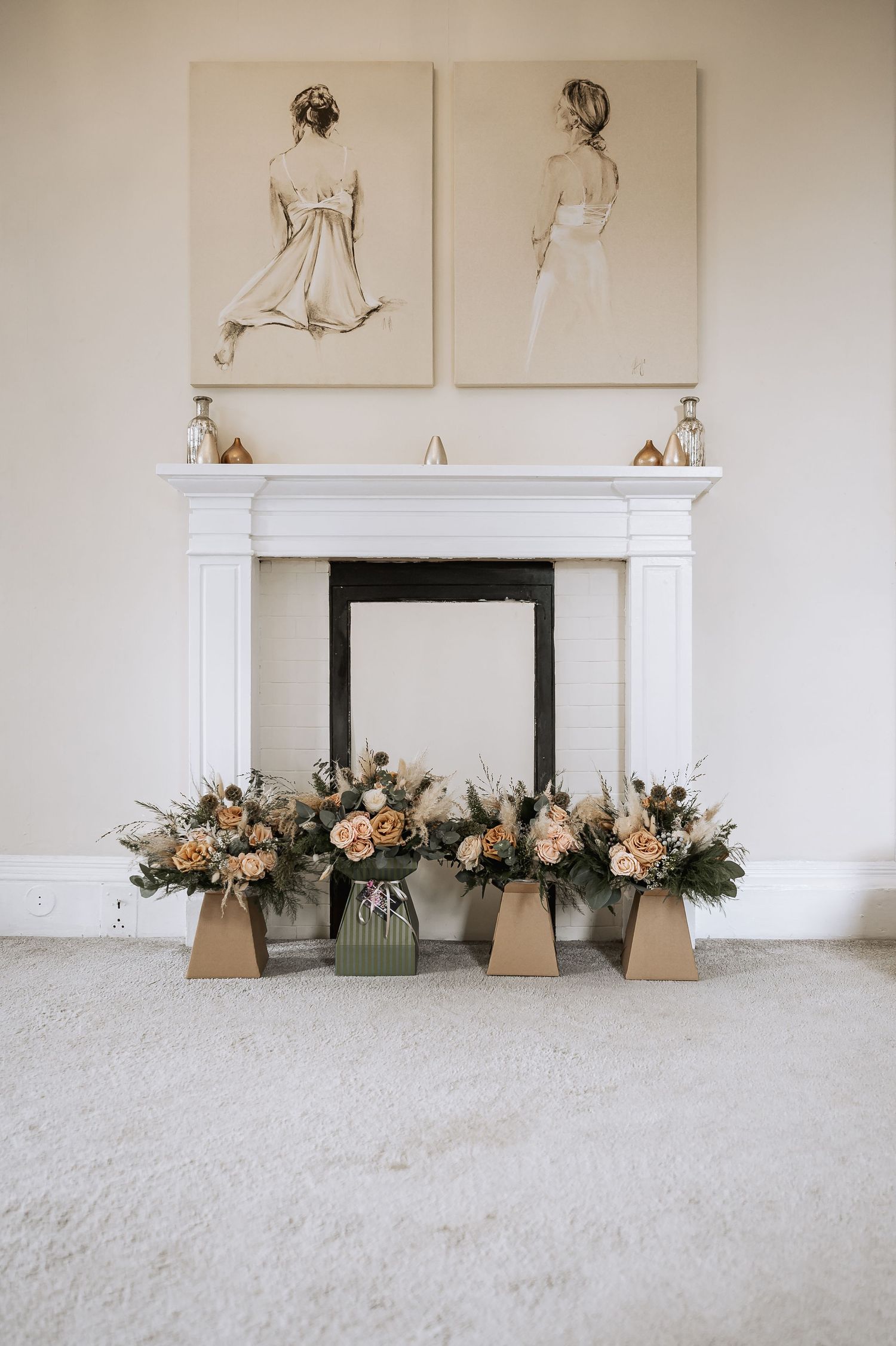 Peach floral wedding arrangements displayed before a white fireplace with fashion artwork above.