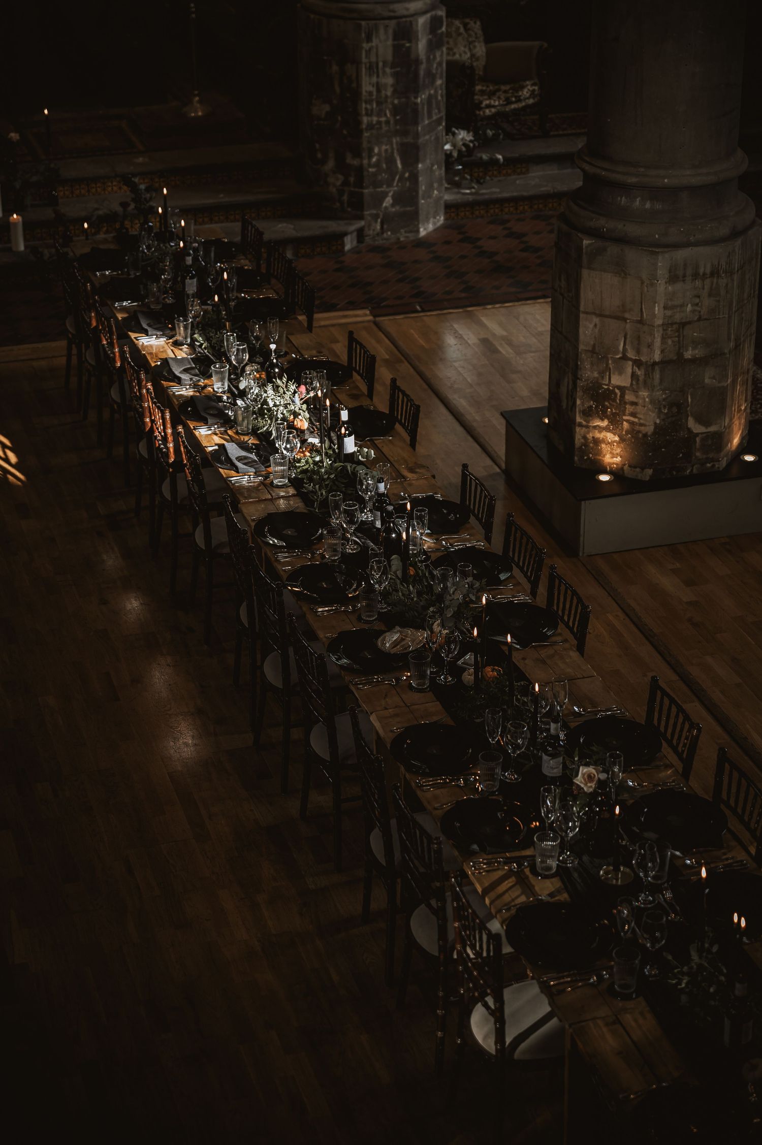 Aerial view of long rustic wedding reception tables with dark moody candlelit decor in a church venue.