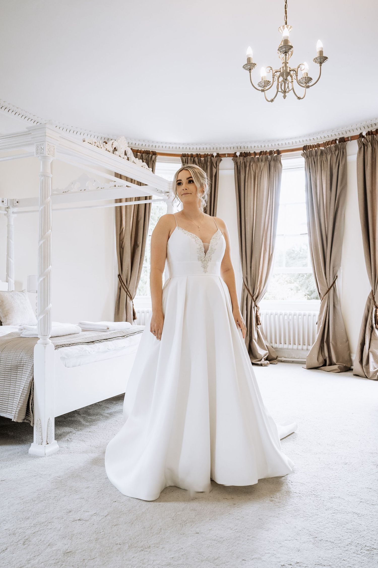 Bride in a strapless ball gown wedding dress poses in a luxurious four-poster bedroom suite.