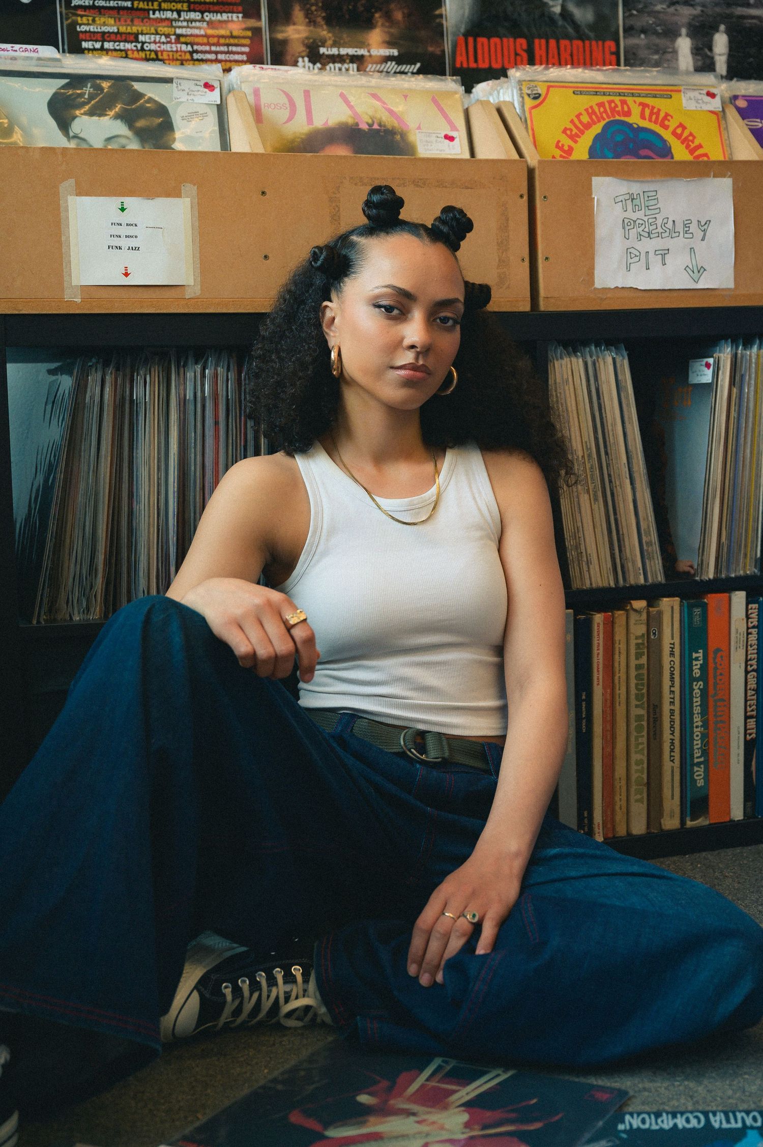 Young woman with curly hair sitting on floor in front of vinyl record shelves in music store.