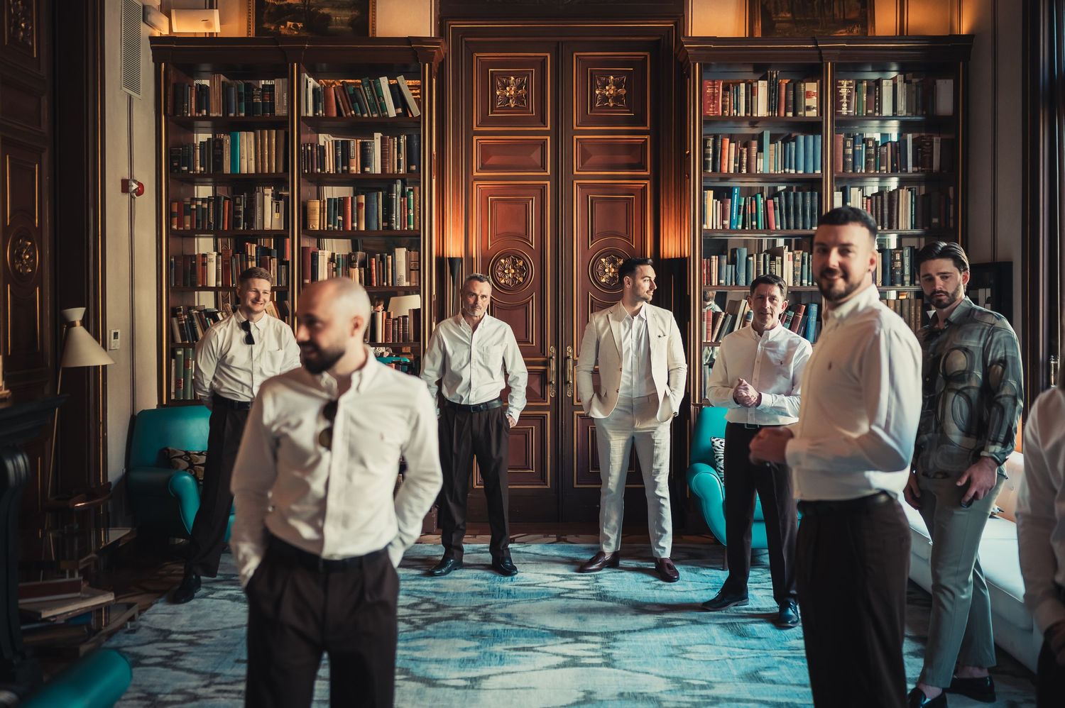 Groomsmen gathered in elegant library room with wooden bookshelves before wedding ceremony.