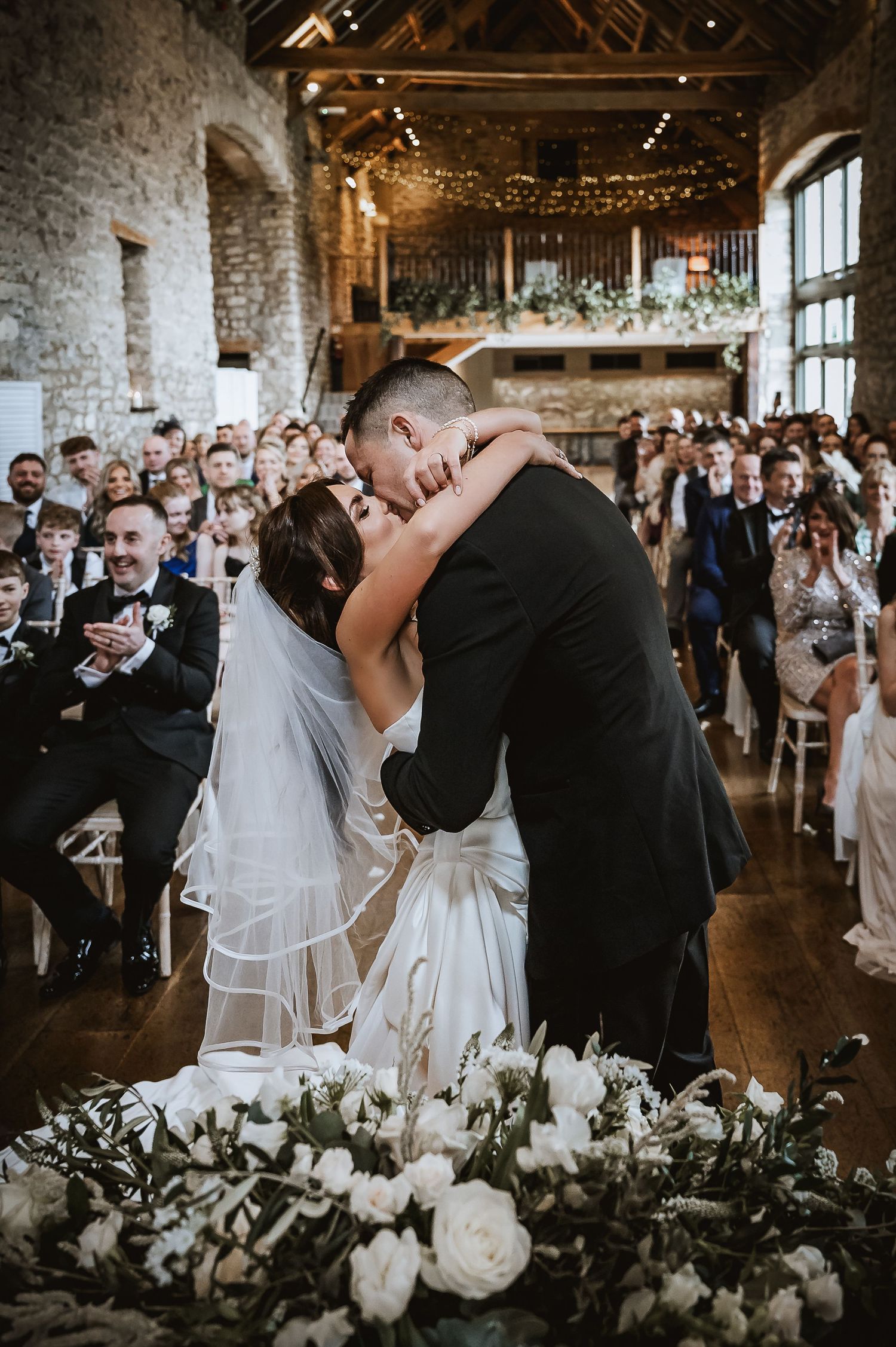 Bride and groom share their first kiss at the altar in a rustic barn wedding venue.