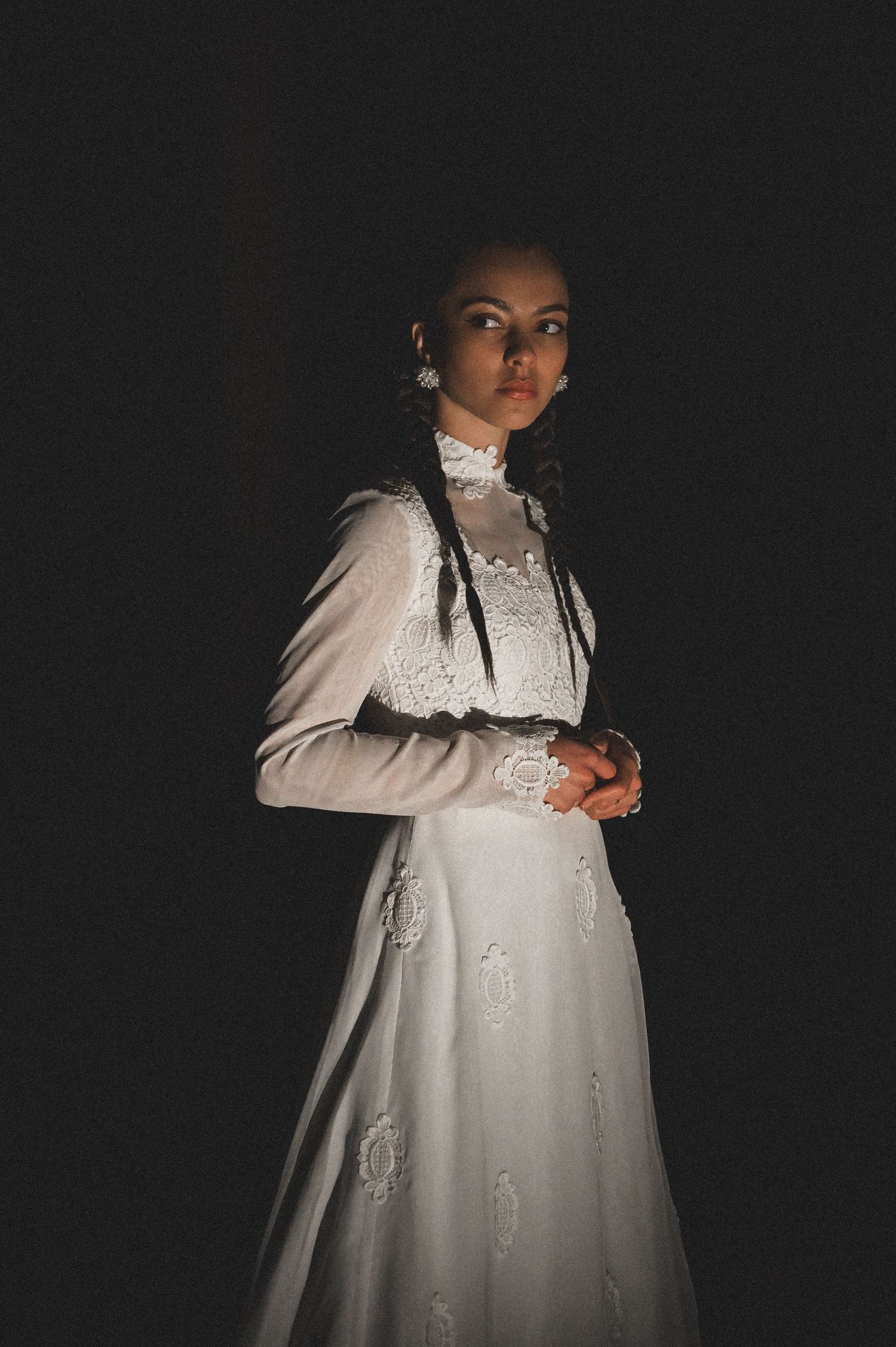 Woman in ornate white Victorian dress posing dramatically against black background.