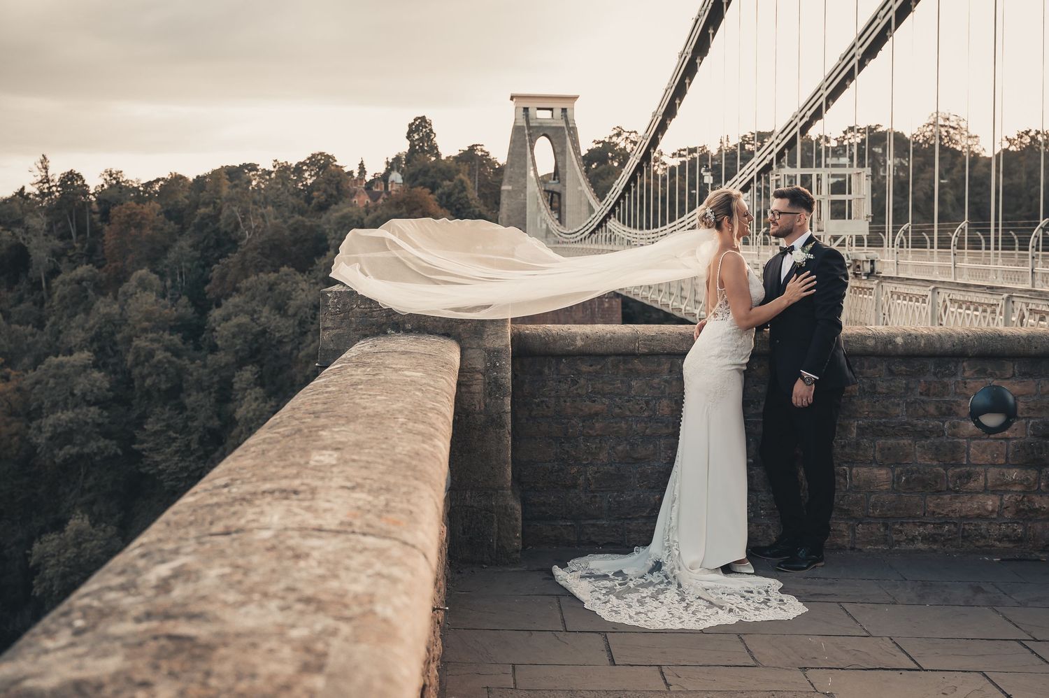 Bride's veil blows in the wind as couple kiss on the Clifton Suspension Bridge viewpoint.
