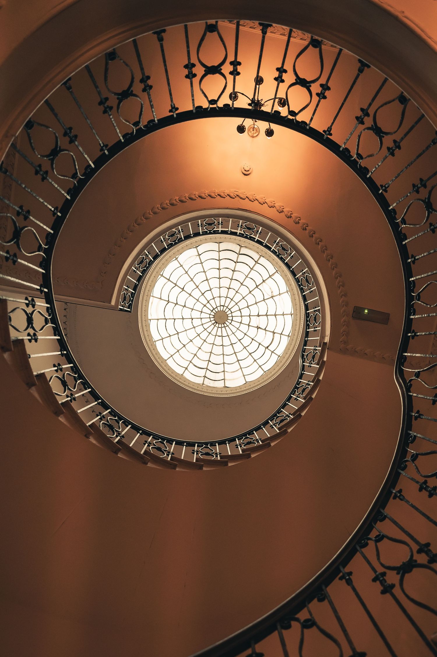 Stunning spiral staircase with ornate black iron railings and circular skylight viewed from below.