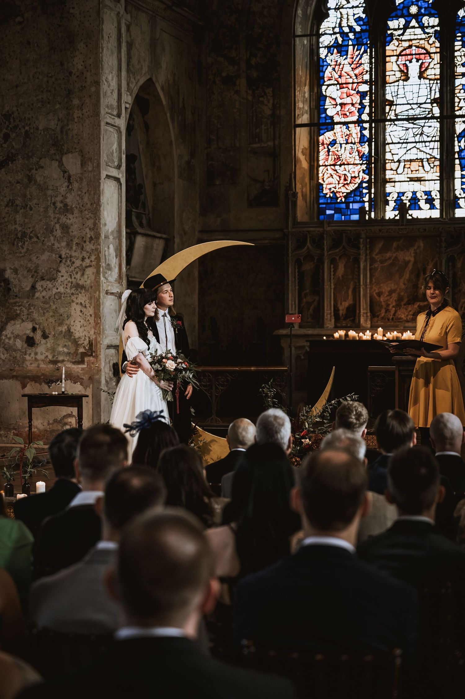 Bride and groom at altar with crescent moon decor in candlelit gothic church ceremony.