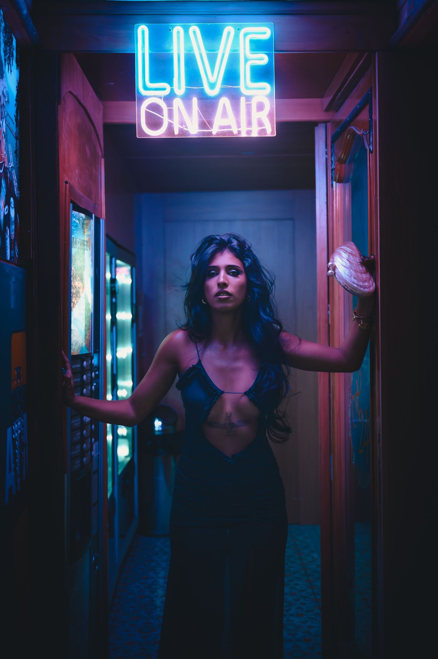 Woman in black dress standing under neon Live On Air sign in dimly lit corridor.