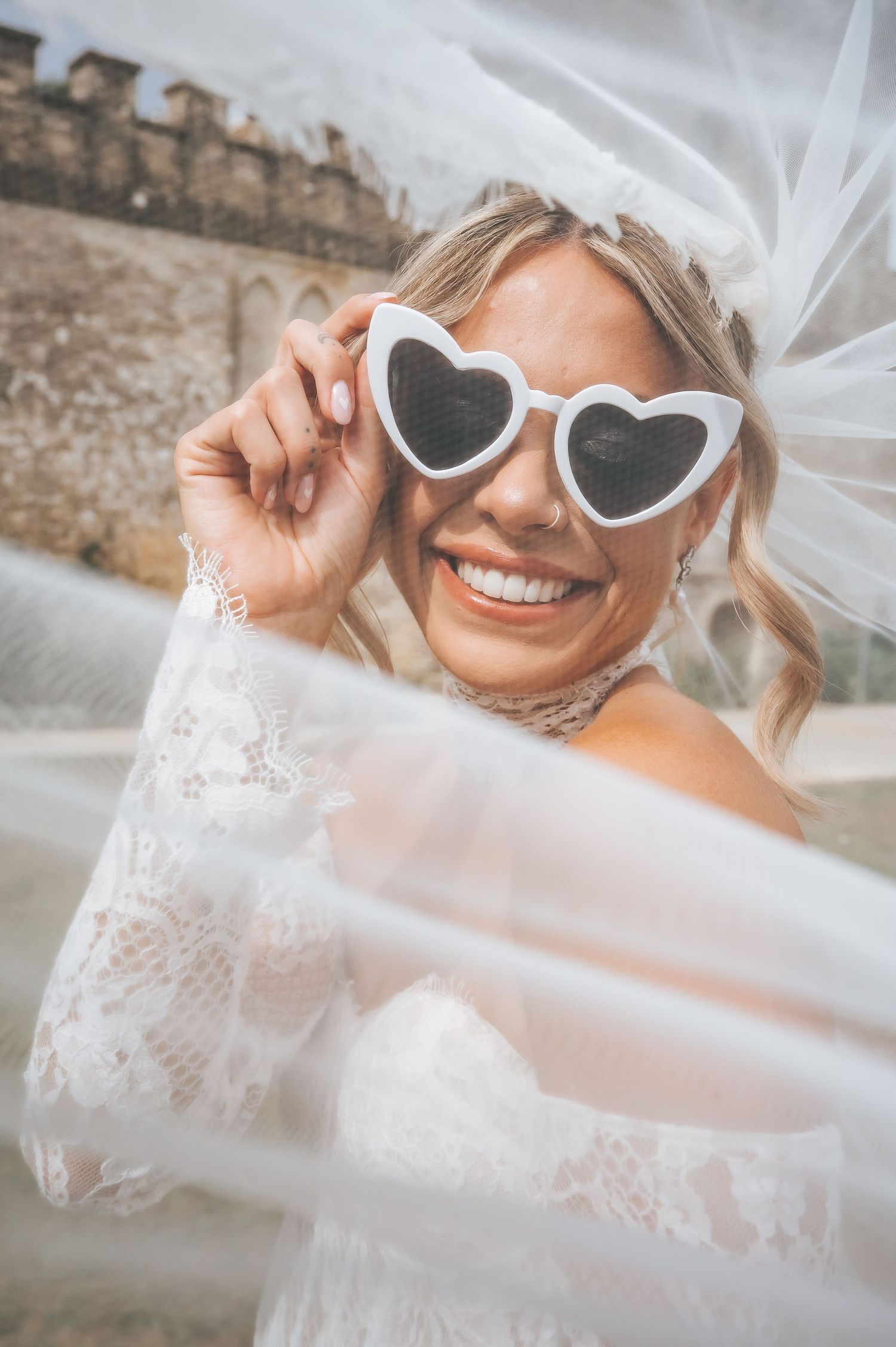 Smiling bride wearing heart-shaped white sunglasses and a veil on her wedding day.