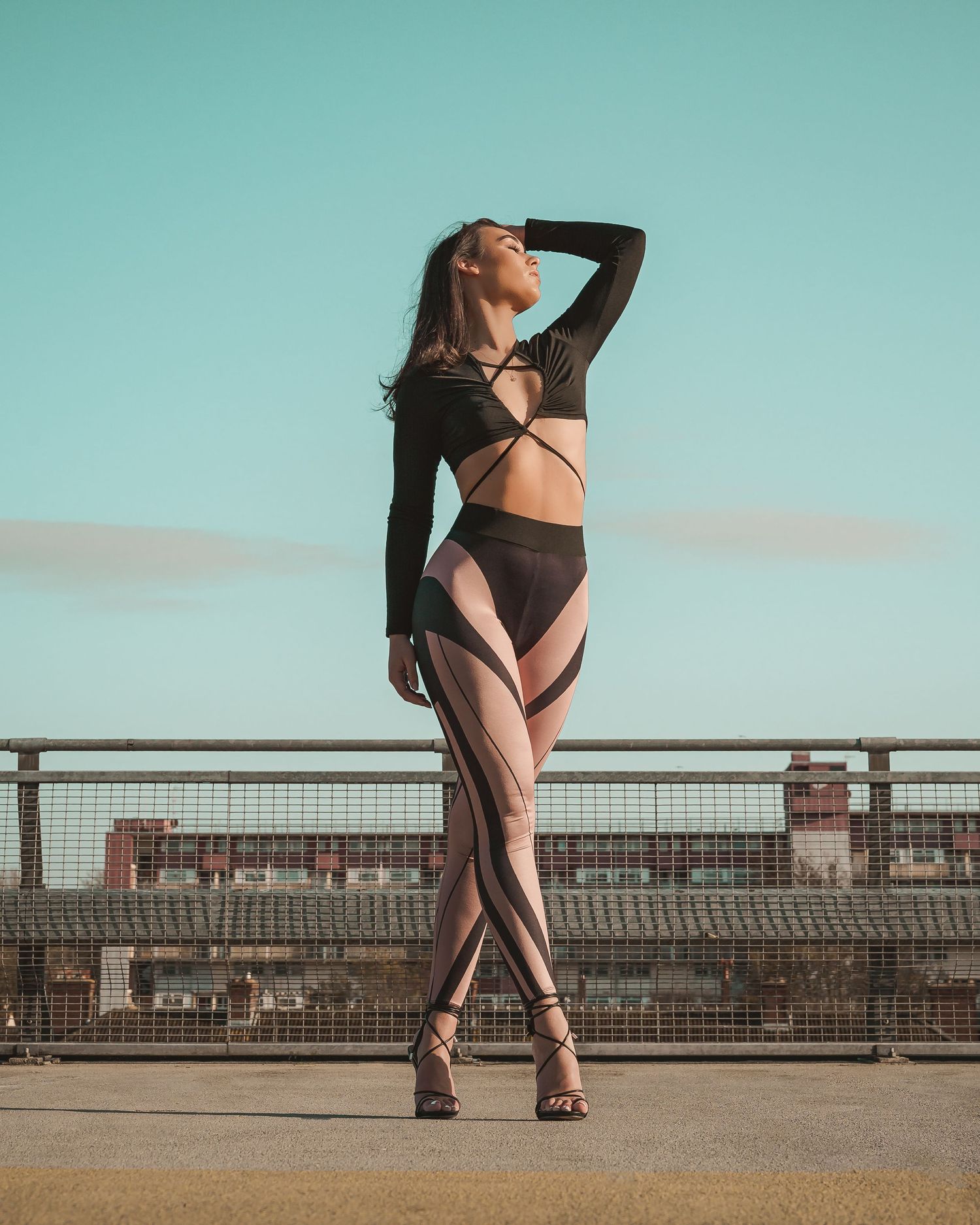 Woman in black strappy crop top and geometric sheer pants posing on urban rooftop.