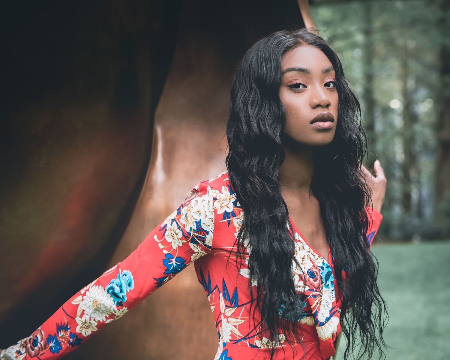 Young woman in red floral outfit posing outdoors beside a large bronze sculpture.