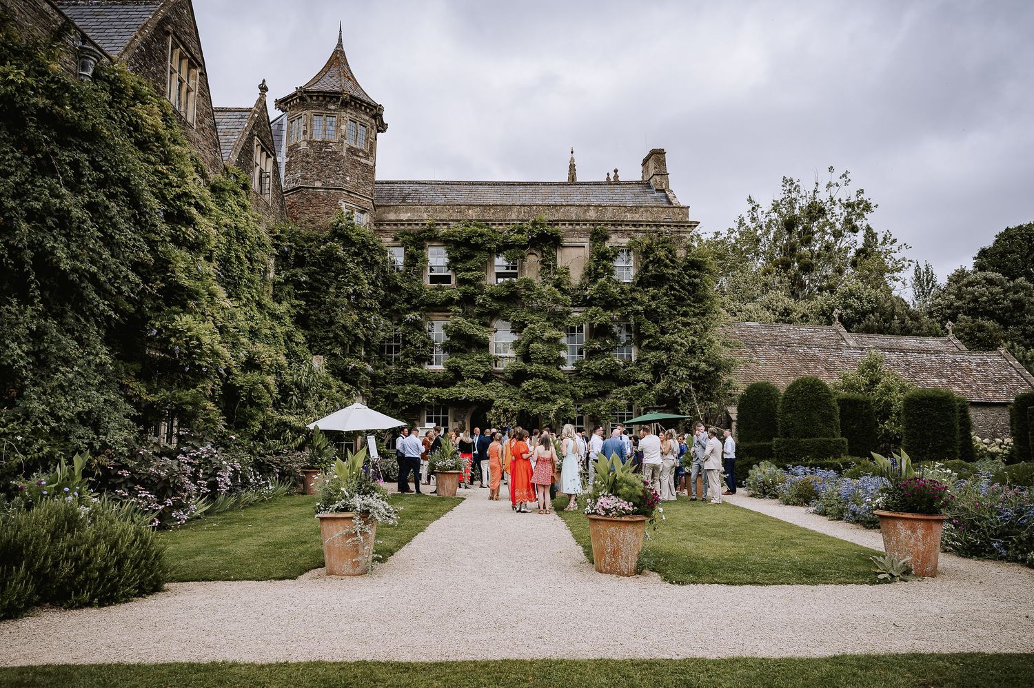Wedding guests mingle in the gardens of an ivy-covered English manor house venue.
