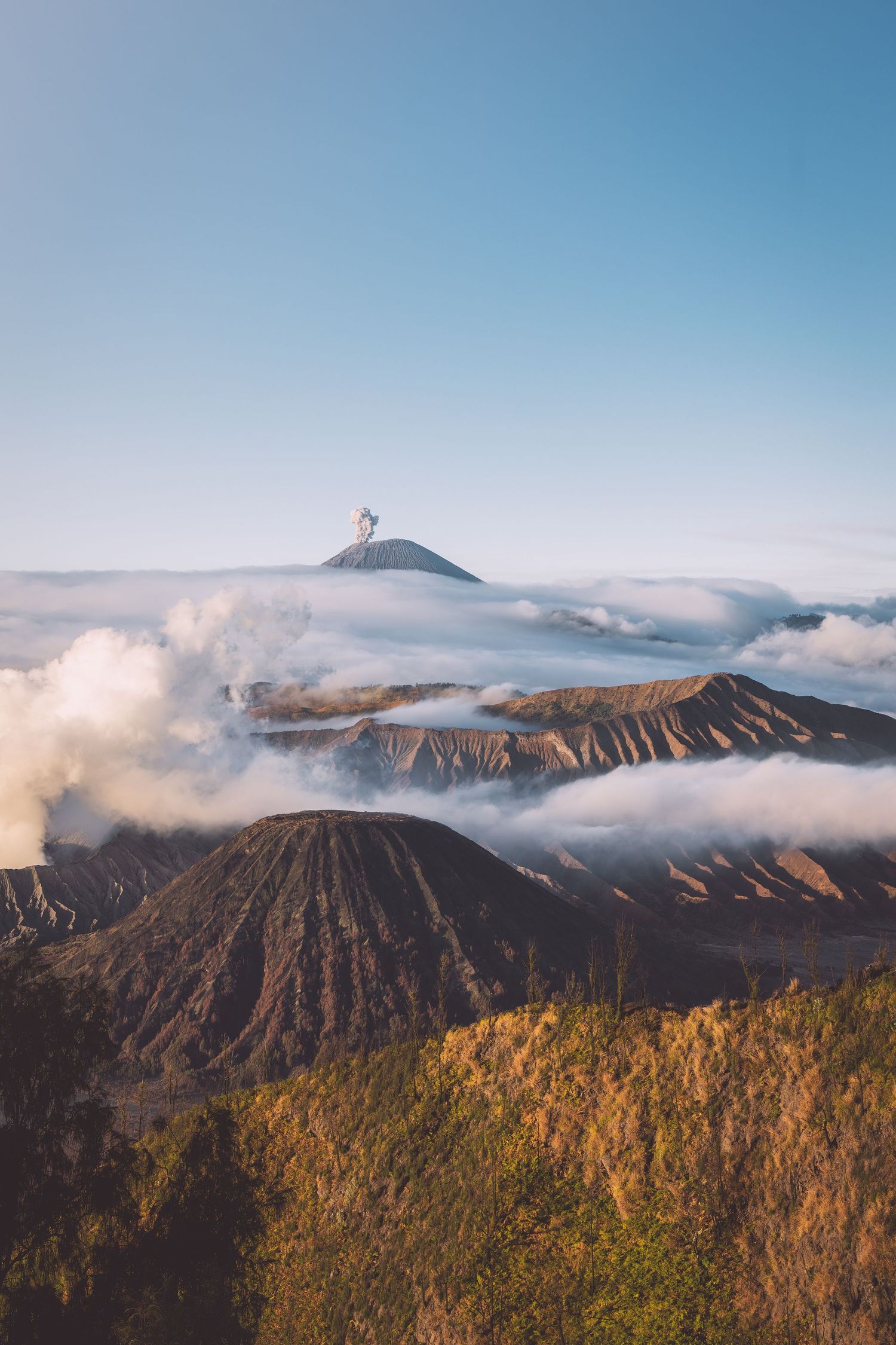 Majestic volcanic landscape with steam rising from Mount Bromo crater amidst misty clouds in Indonesia.