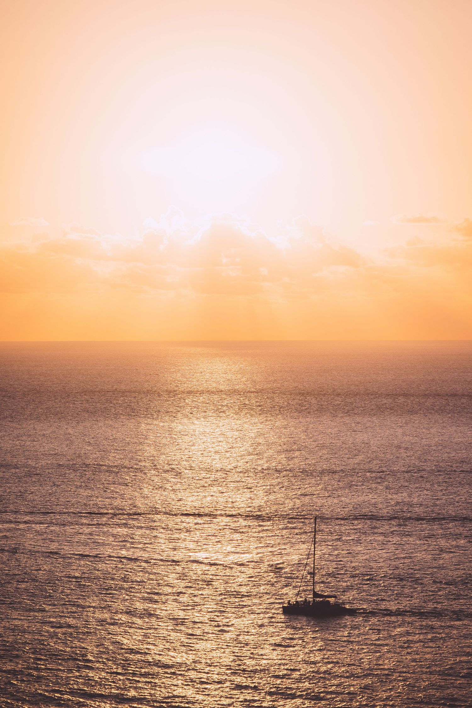 Sailboat floats on golden ocean waters during a vibrant sunset in Reunion island.