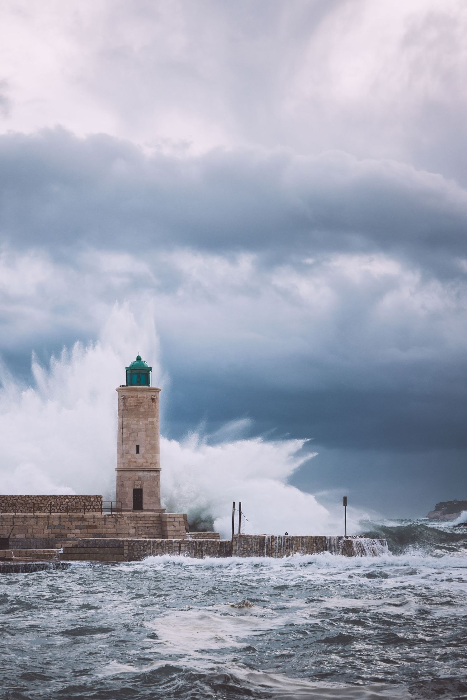 Massive waves crash against a lighthouse and seawall during stormy weather at sea in Cassis, France.