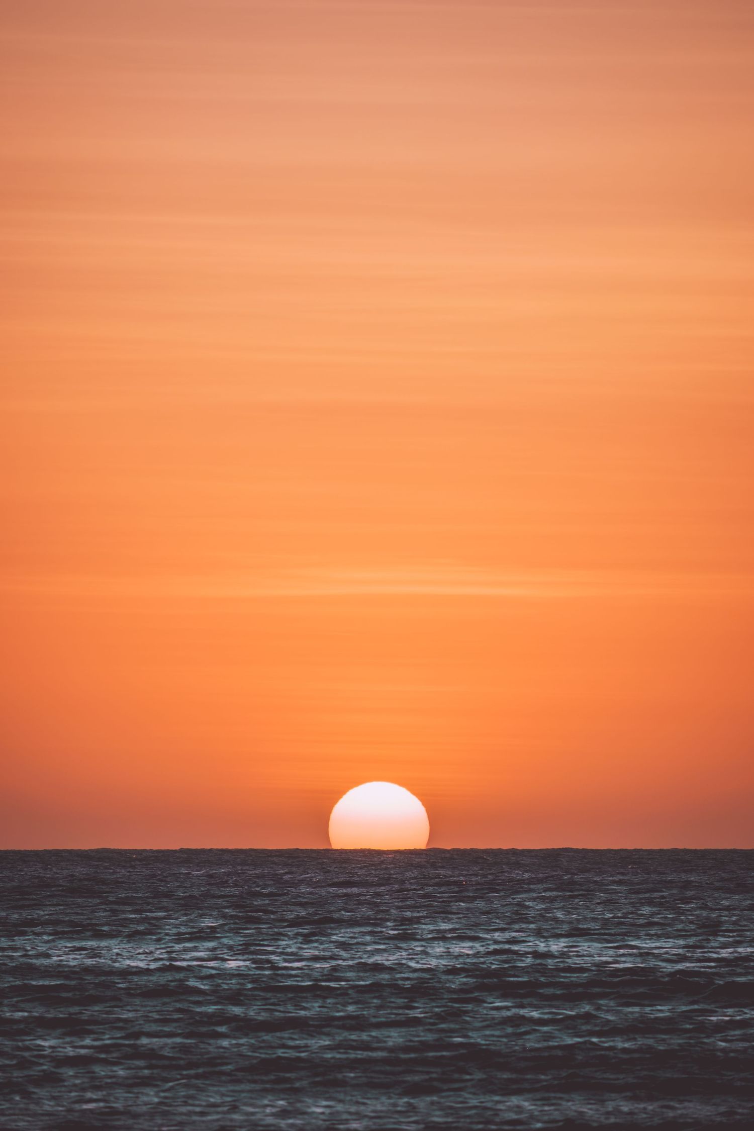 Dramatic orange sunset over dark ocean waters with sun touching the horizon in Jericoacoara in Brazil.