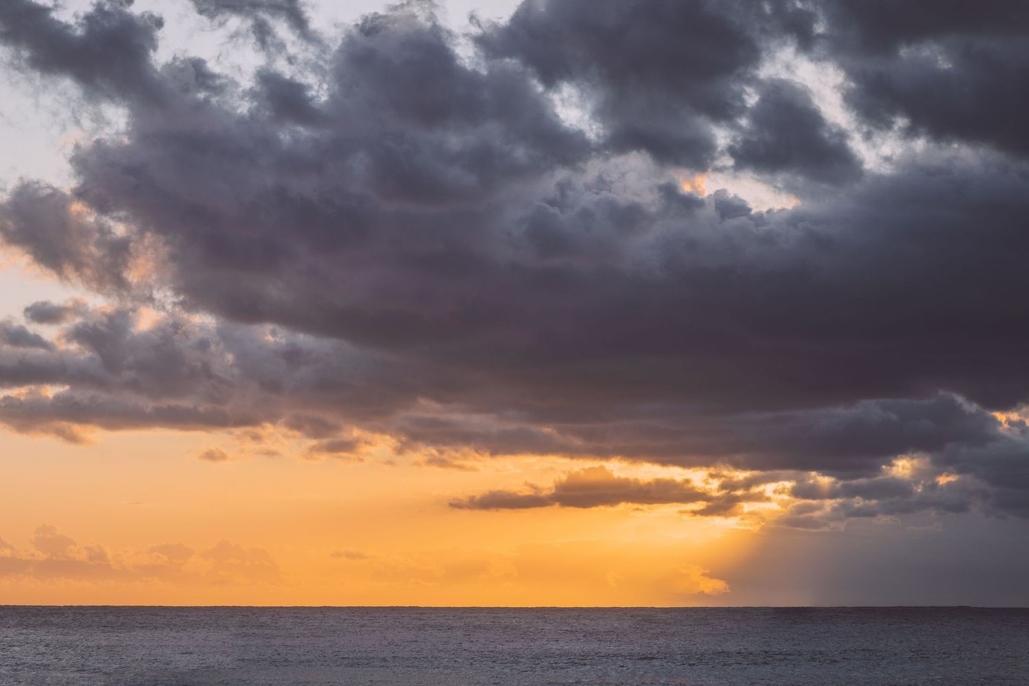 Dramatic orange sunset sky with dark storm clouds over calm ocean waters in Reunion island.