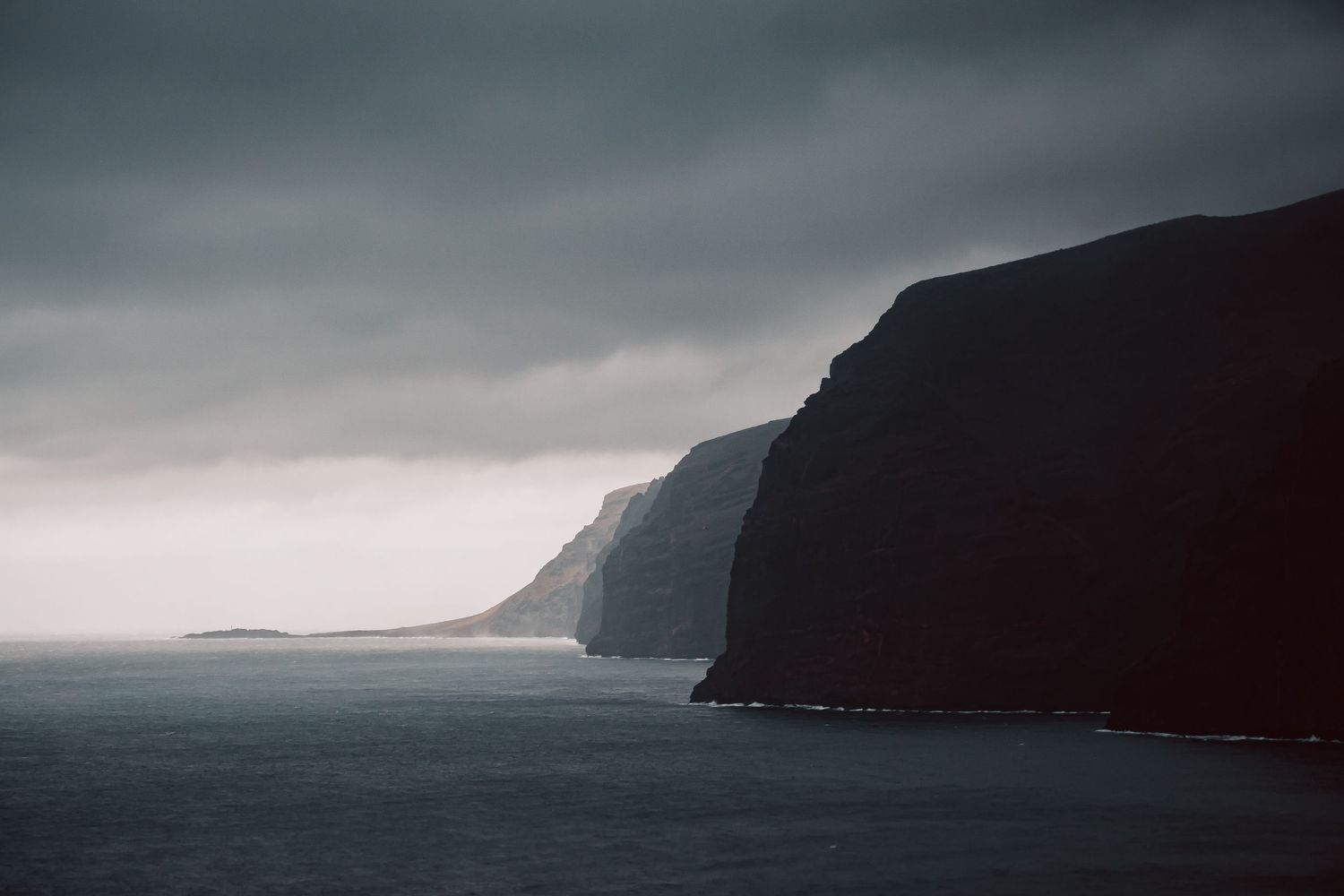 Moody coastal cliffs rising from misty ocean under dark cloudy skies in Tenerife.