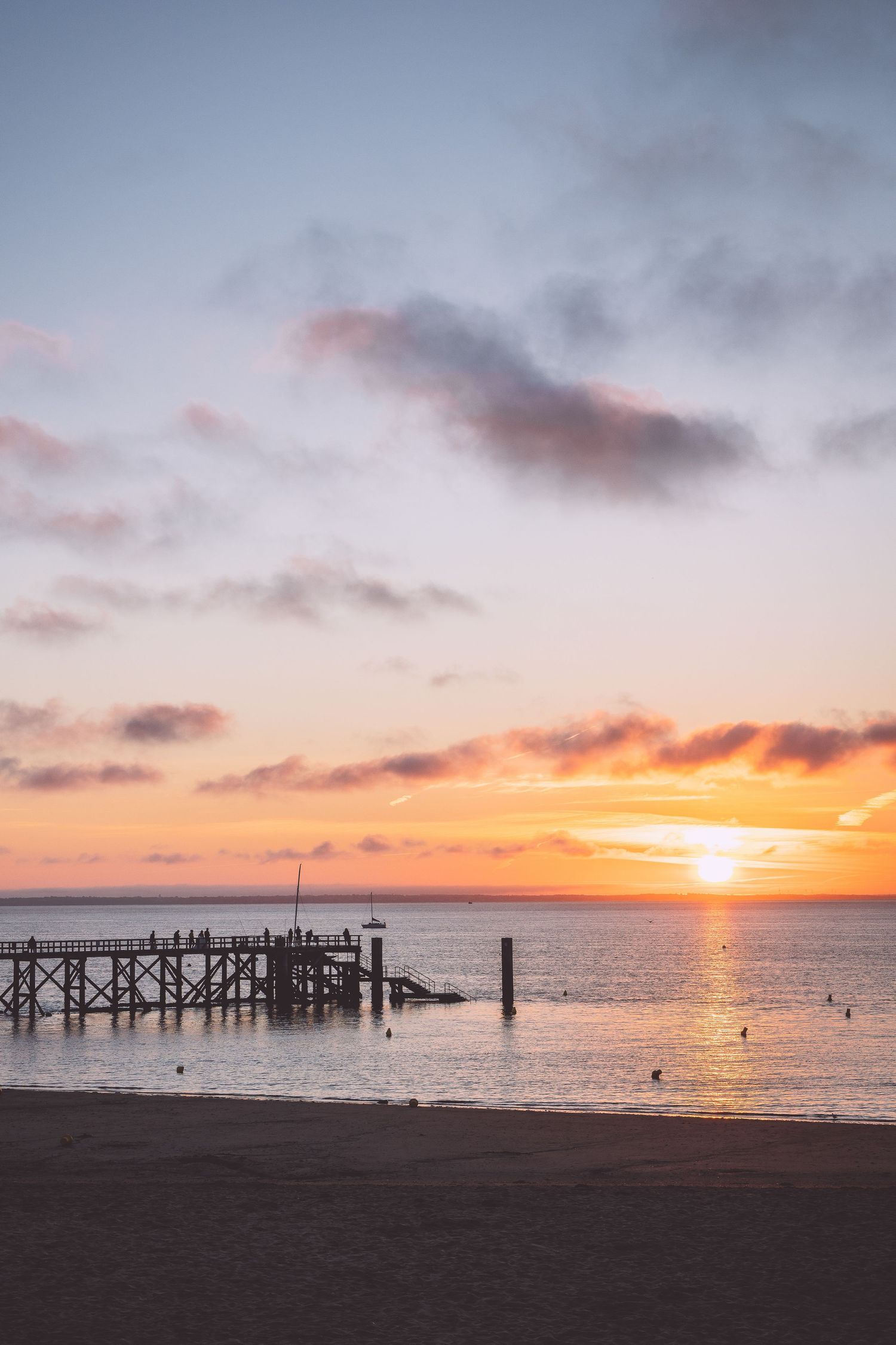 Vibrant orange sunset over the ocean with a wooden pier silhouetted against the colorful sky in Noirmoutier, France.