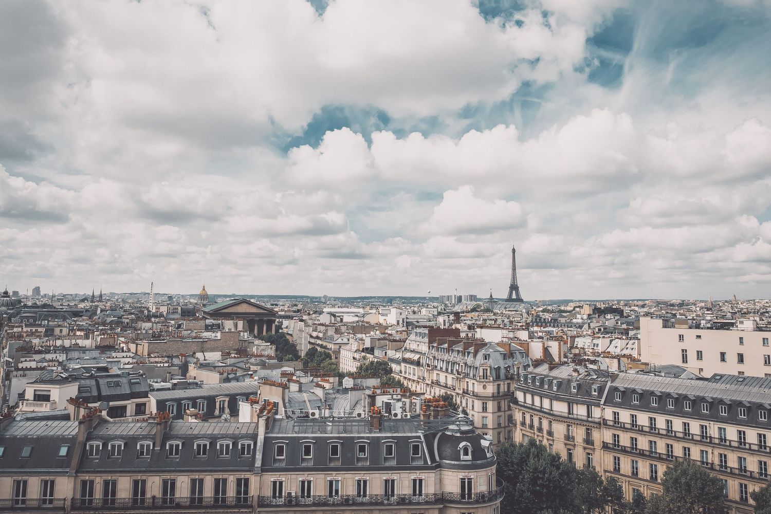 Panoramic view of Paris rooftops and architecture under cloudy skies.