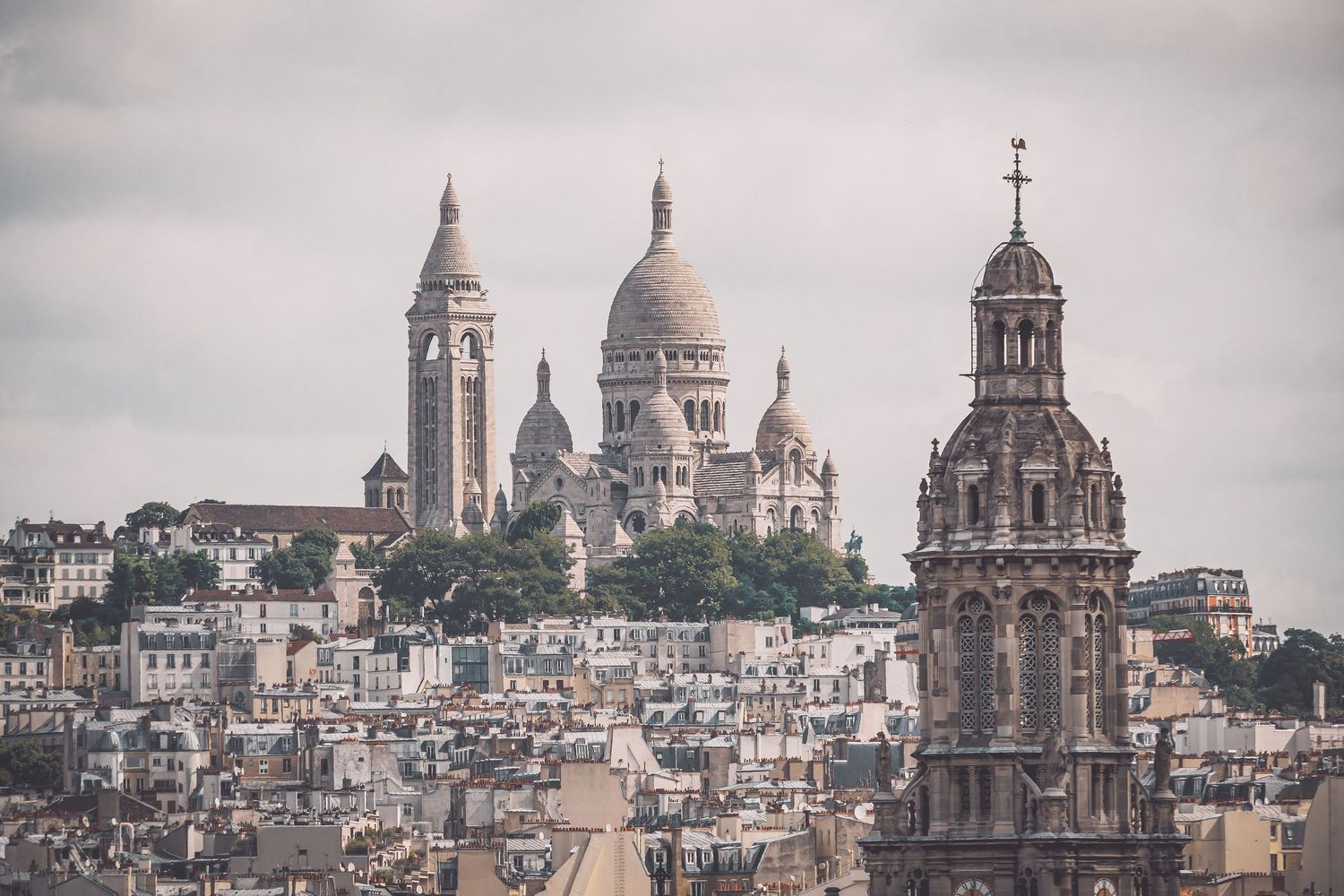 Architectural details of Sacré-Cœur's domes and towers against overcast sky.