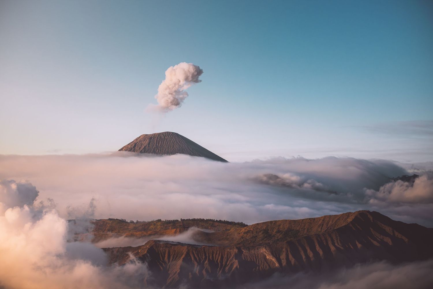 Majestic volcanic landscape with steam rising from Mount Bromo crater amidst misty clouds in Indonesia.