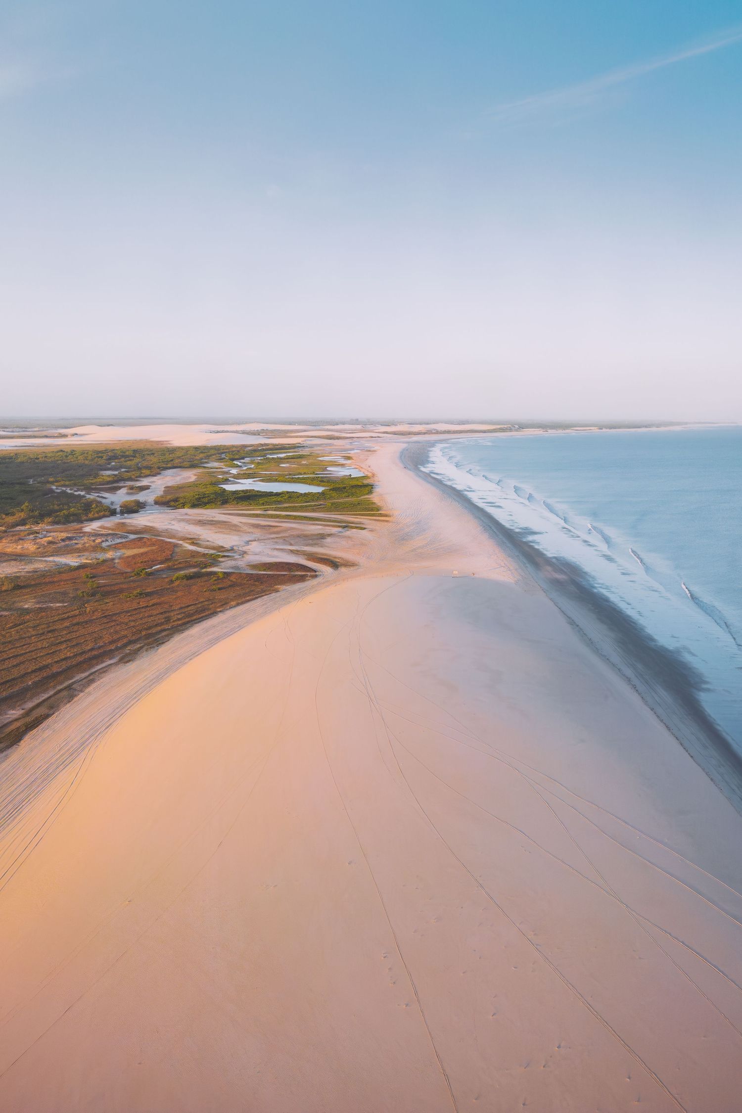 Aerial view of sandy coastline where river meets ocean with pristine beach stretching into distance in Jericoacoara in Brazil.