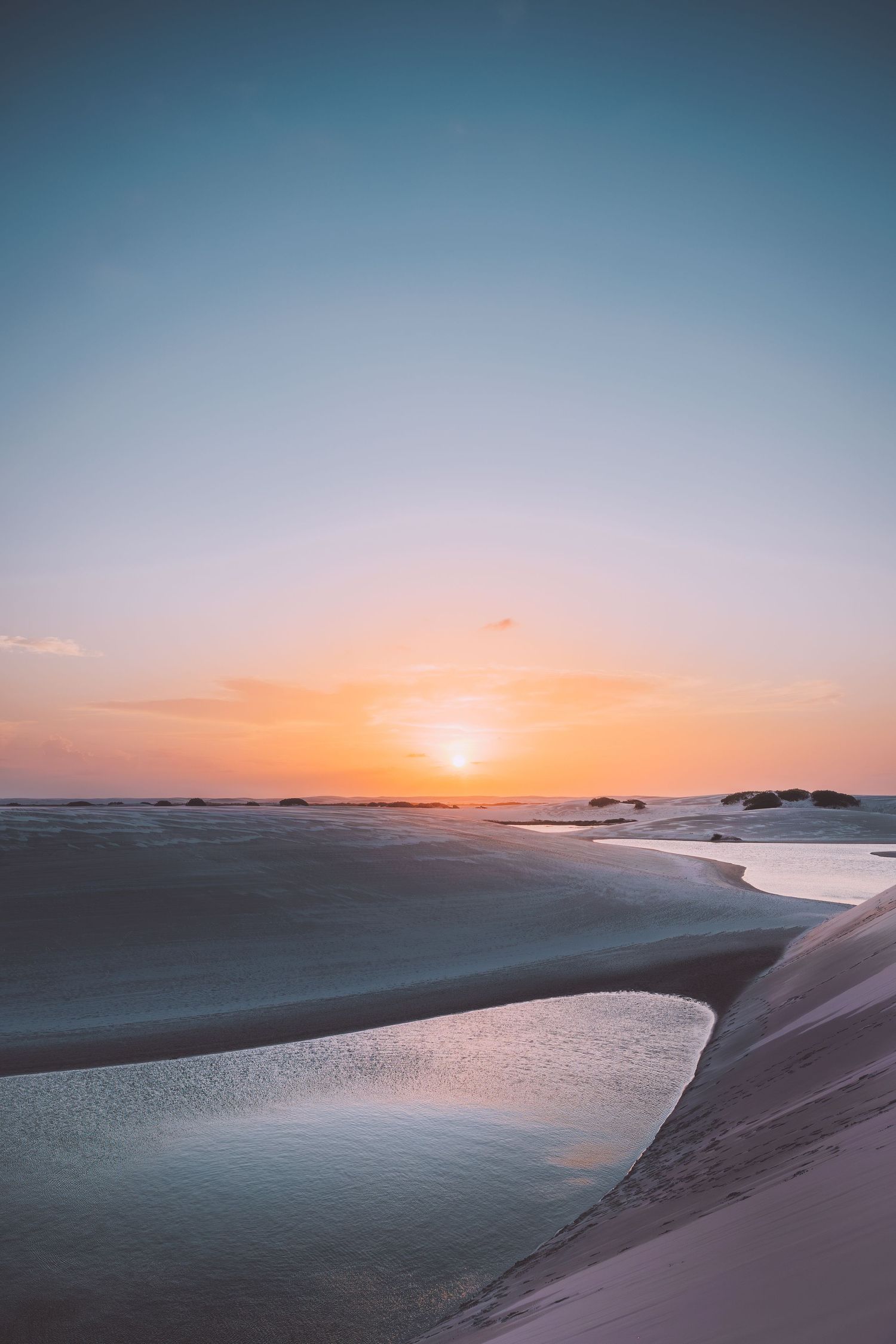 Coastal sand dunes meeting the ocean at sunset with golden light on the horizon in Lençois desert in Brazil.