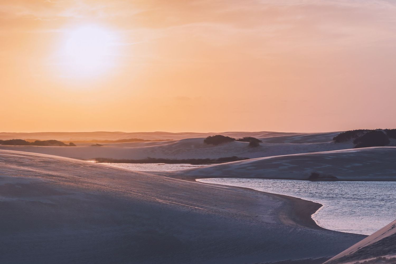 Scenic coastal dunes and beach stretching along calm waters during golden hour in Lençois desert in Brazil.