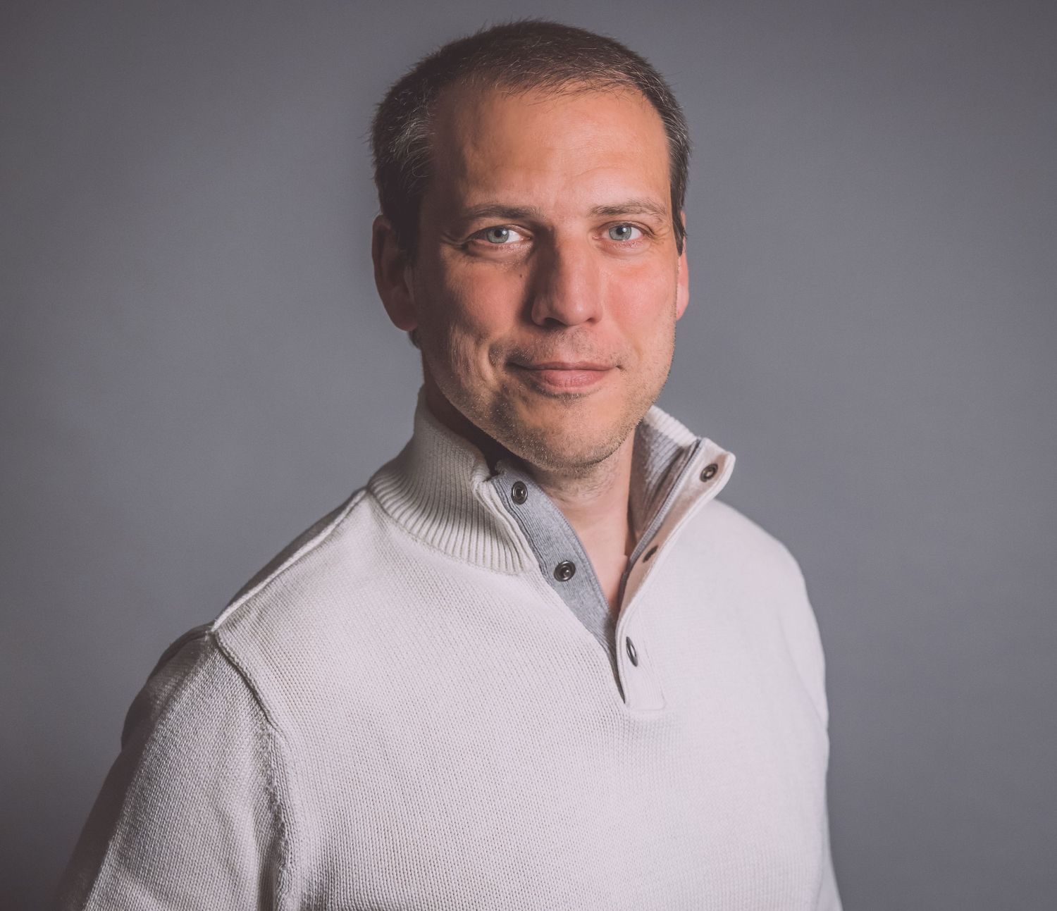 Professional portrait in white sweater against grey background.
