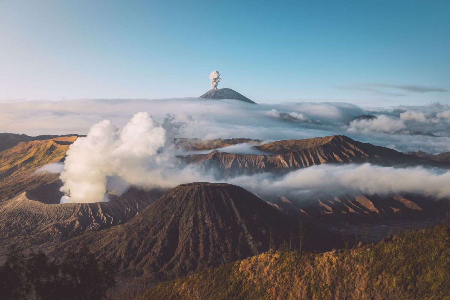 Majestic volcanic landscape with steam rising from Mount Bromo crater amidst misty clouds in Indonesia.