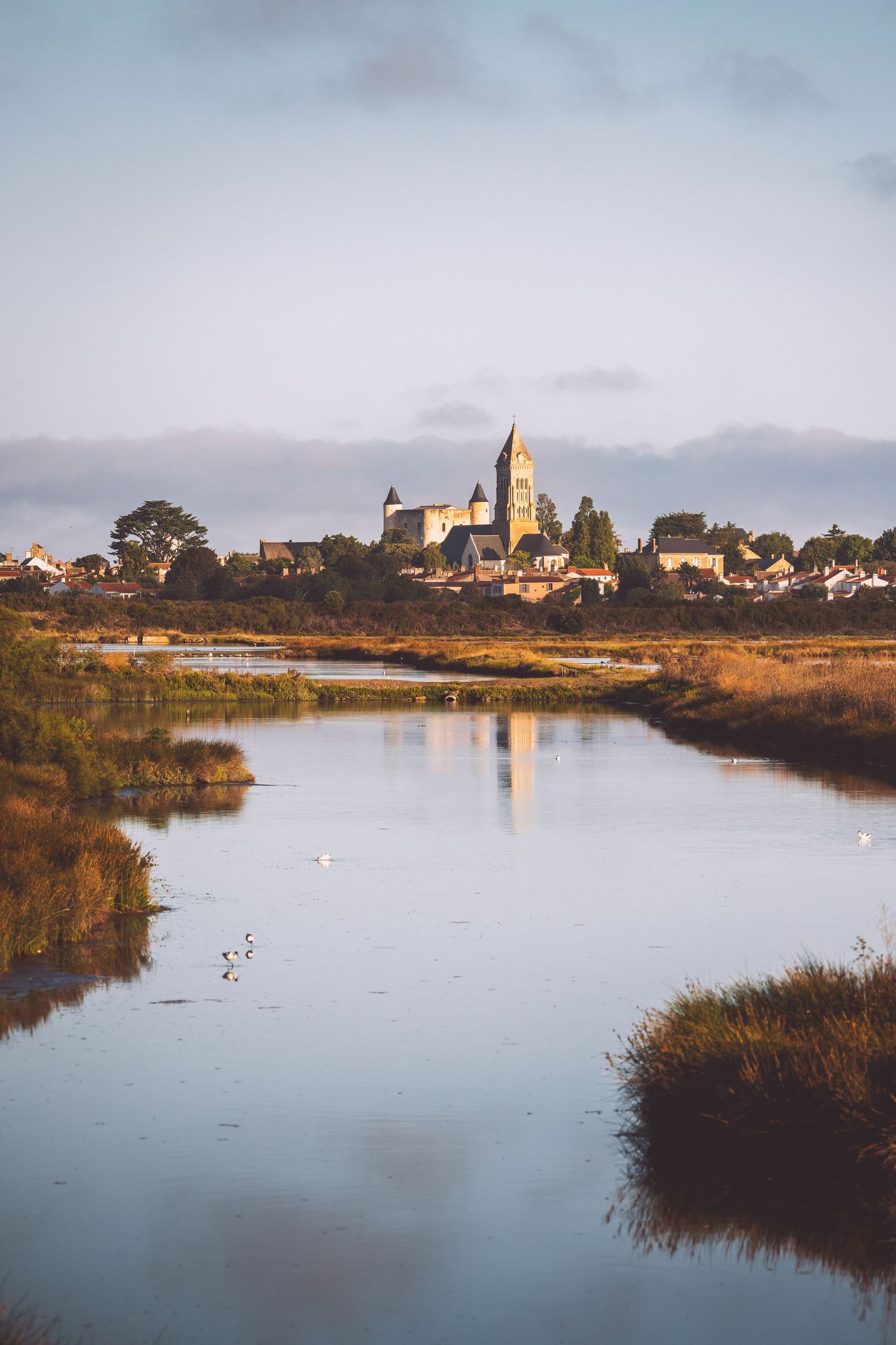 Serene waterscape with a historic church and buildings reflecting in calm waters at dusk in Noirmoutier, France.