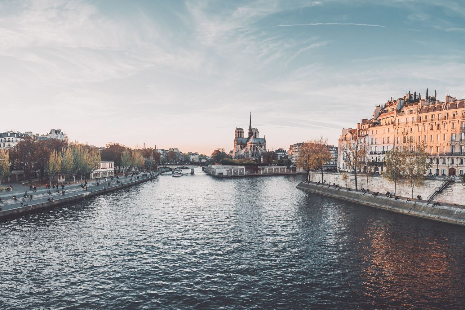 View of the Seine River in Paris with Notre-Dame Cathedral and historic buildings along the riverbanks at sunset.