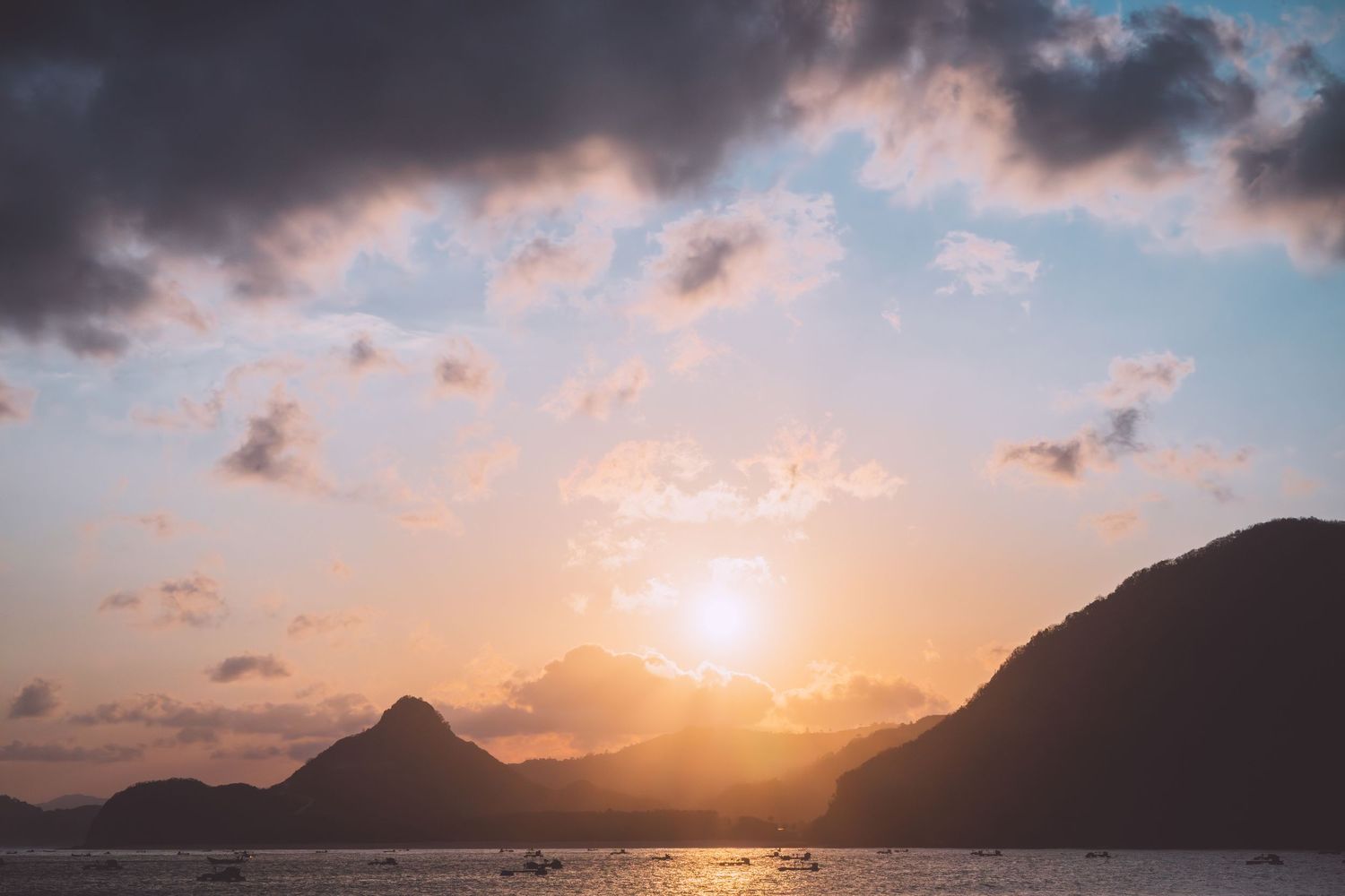 Dramatic mountain silhouettes frame a golden sunset over calm ocean waters in Lombok, Indonesia.