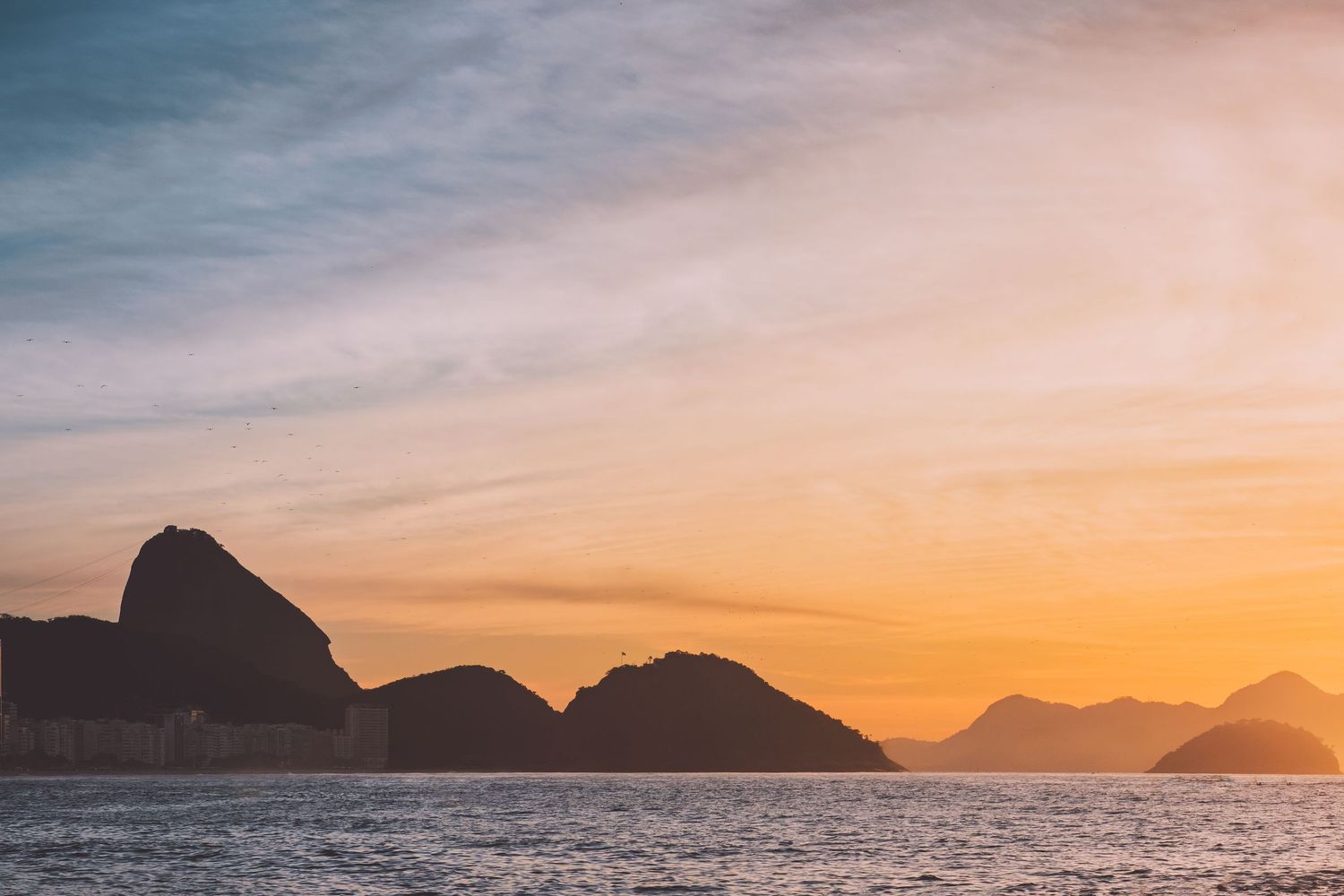 Sunrise seascape with mountain and Sugar Loaf silhouettes reflecting on dark waters in Copacabana, Rio de Janeiro, Brazil.
