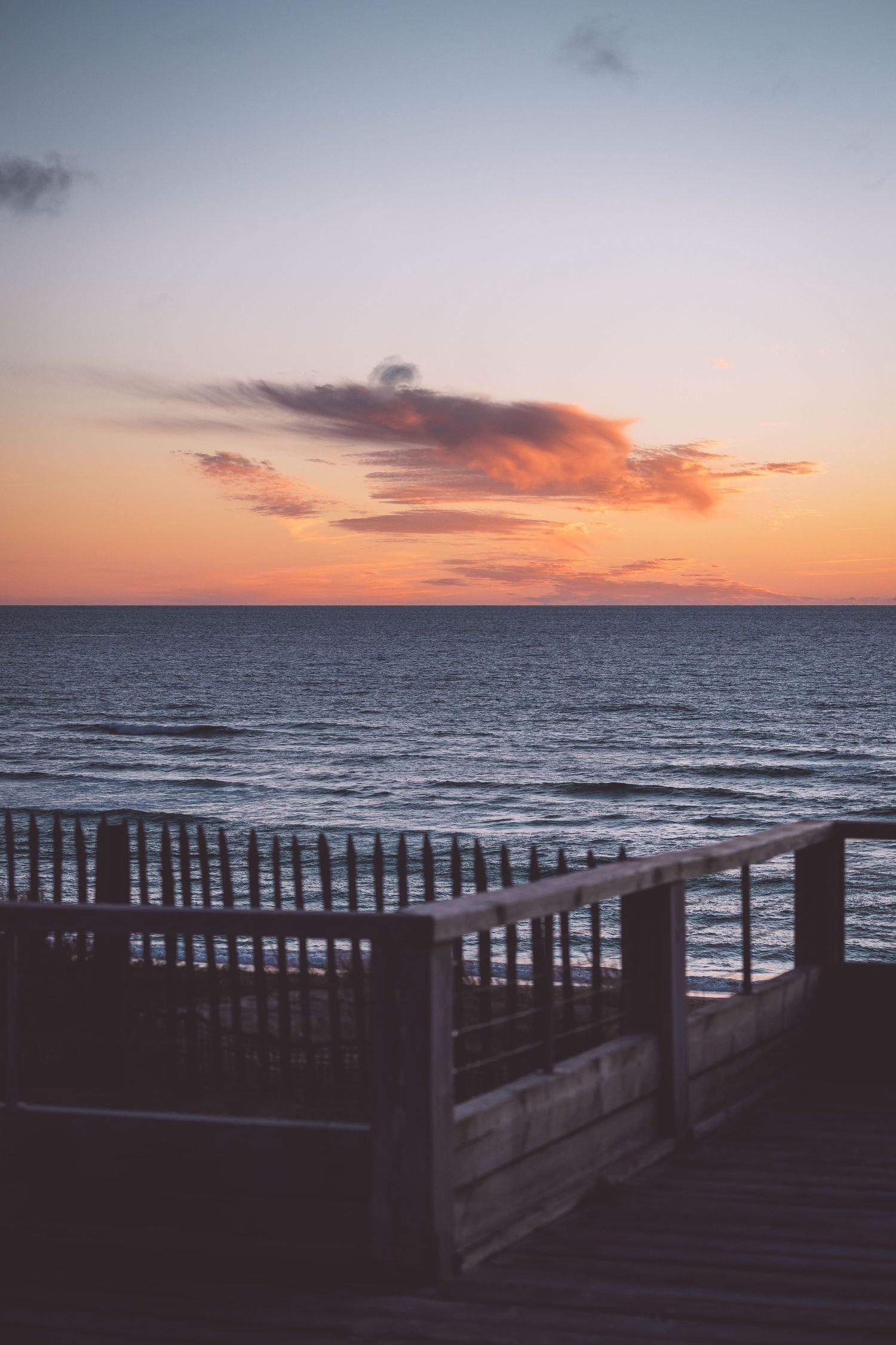 Wooden boardwalk railing silhouetted against a colorful ocean sunset in Mimizan France.