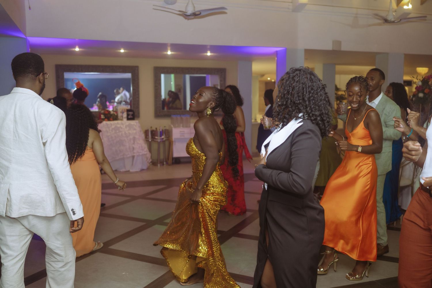 Wedding reception guests mingle and dance in a venue with purple lighting.