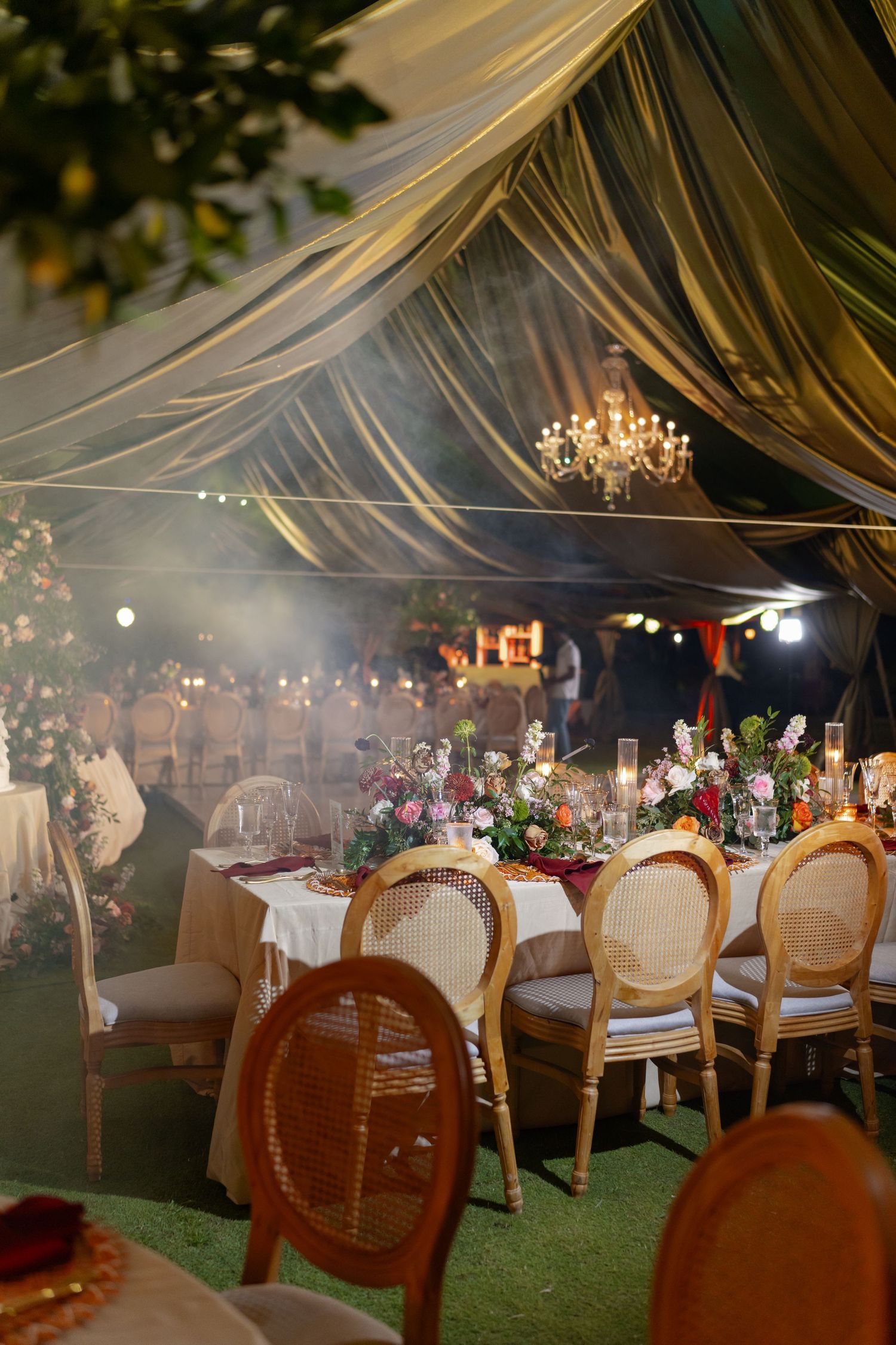 Evening wedding reception setup with draped fabric ceiling and elegant table settings under ambient lighting.